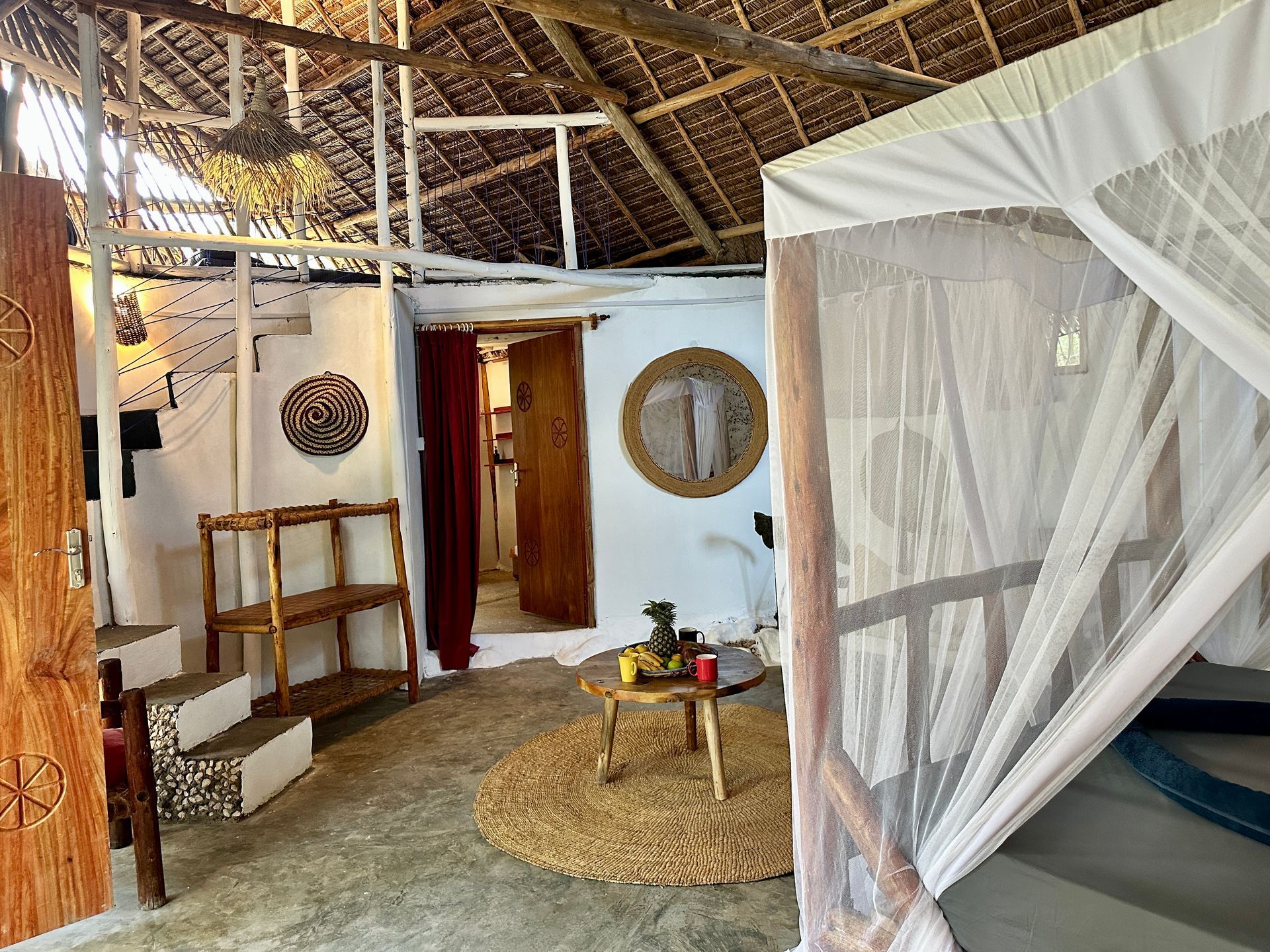 Rustic interior with a bed net, woven rug, and wooden shelves.
