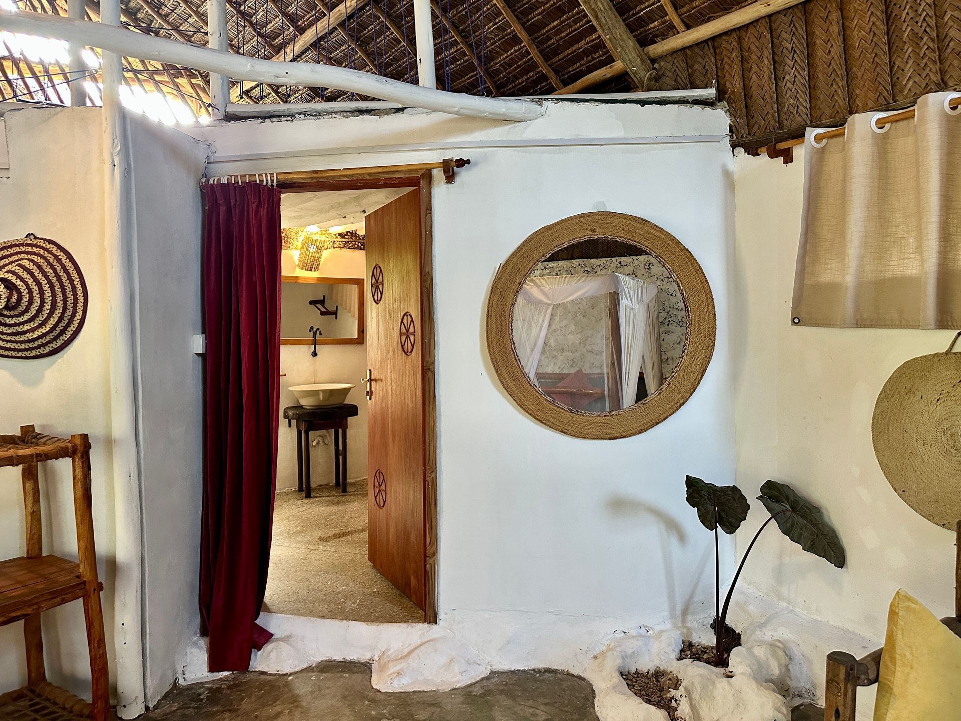 Interior view of a room with an open door to a bathroom; a round mirror and woven decorations.