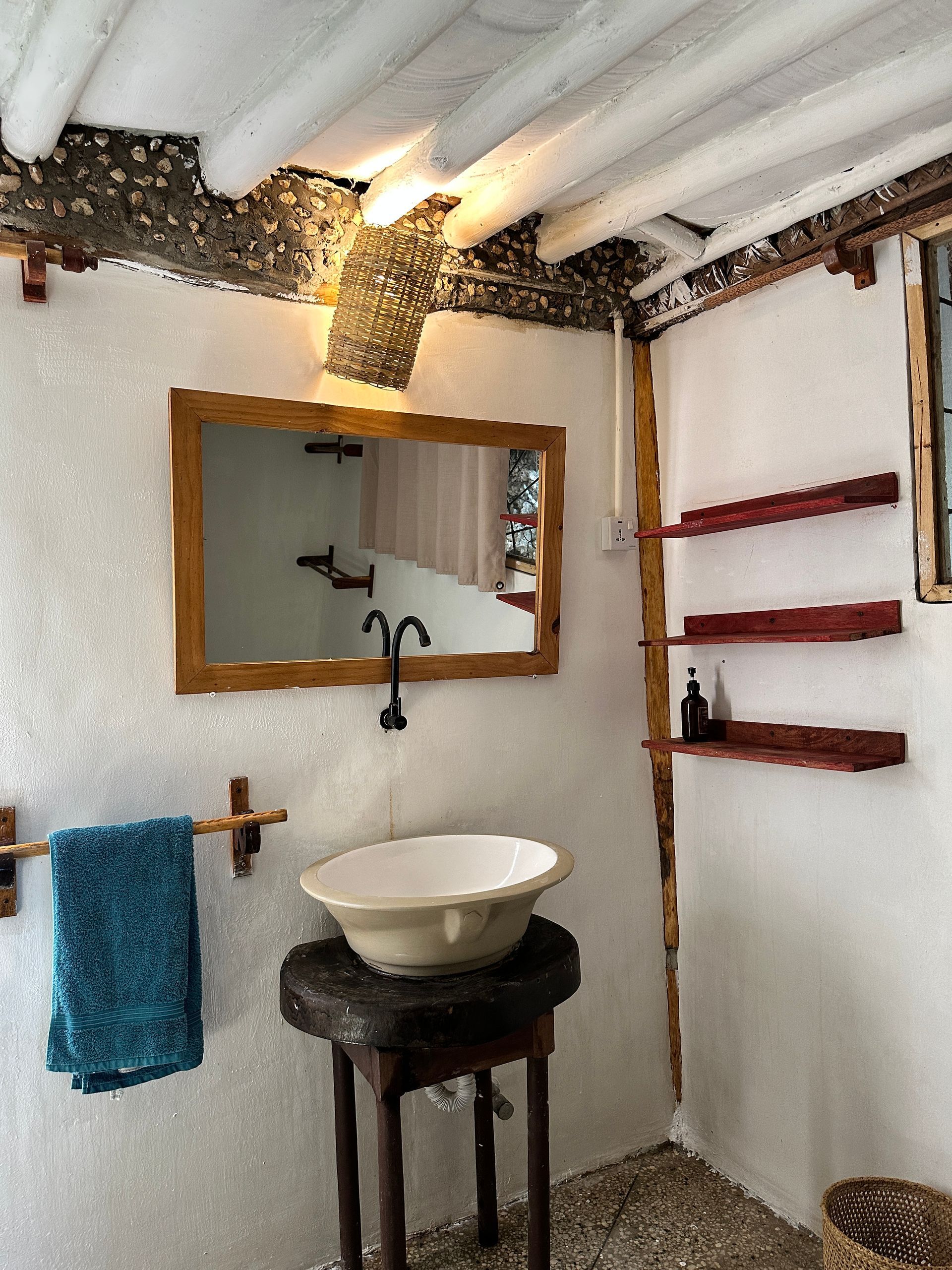 Bathroom with white walls, wooden accents, bowl sink, mirror, and turquoise towel.