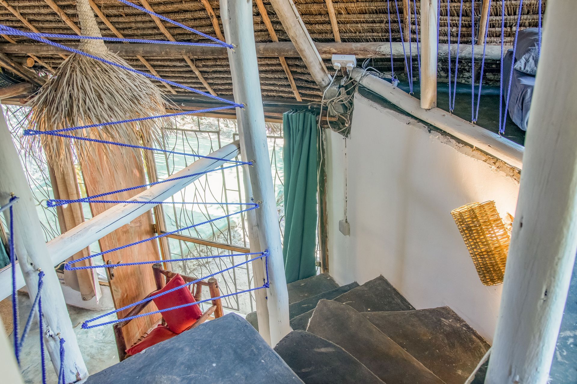 Interior view of a rustic, wooden staircase leading up, with handrails and a thatched roof.
