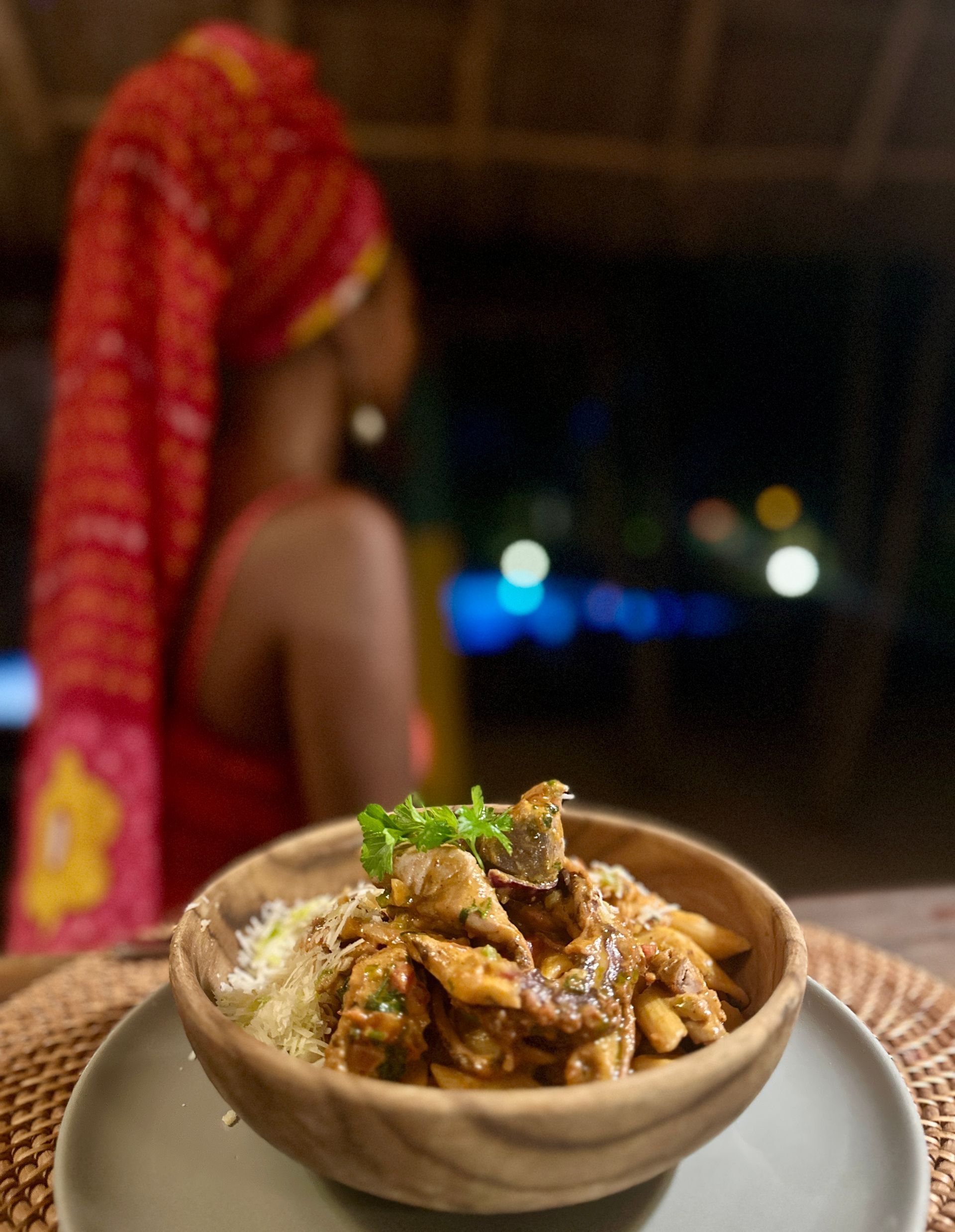 A bowl of food on a plate with a woman in the background.