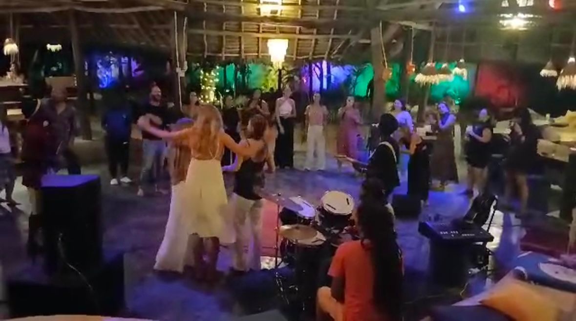 A group of people are dancing in a large room at a party.