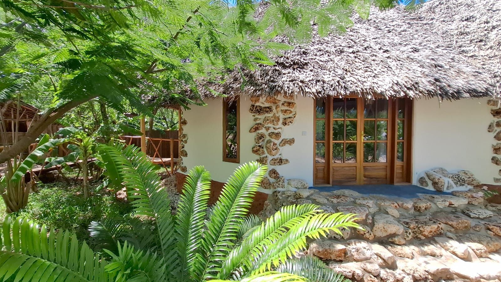 A stone and whitewashed cottage with a thatched roof, surrounded by lush greenery.
