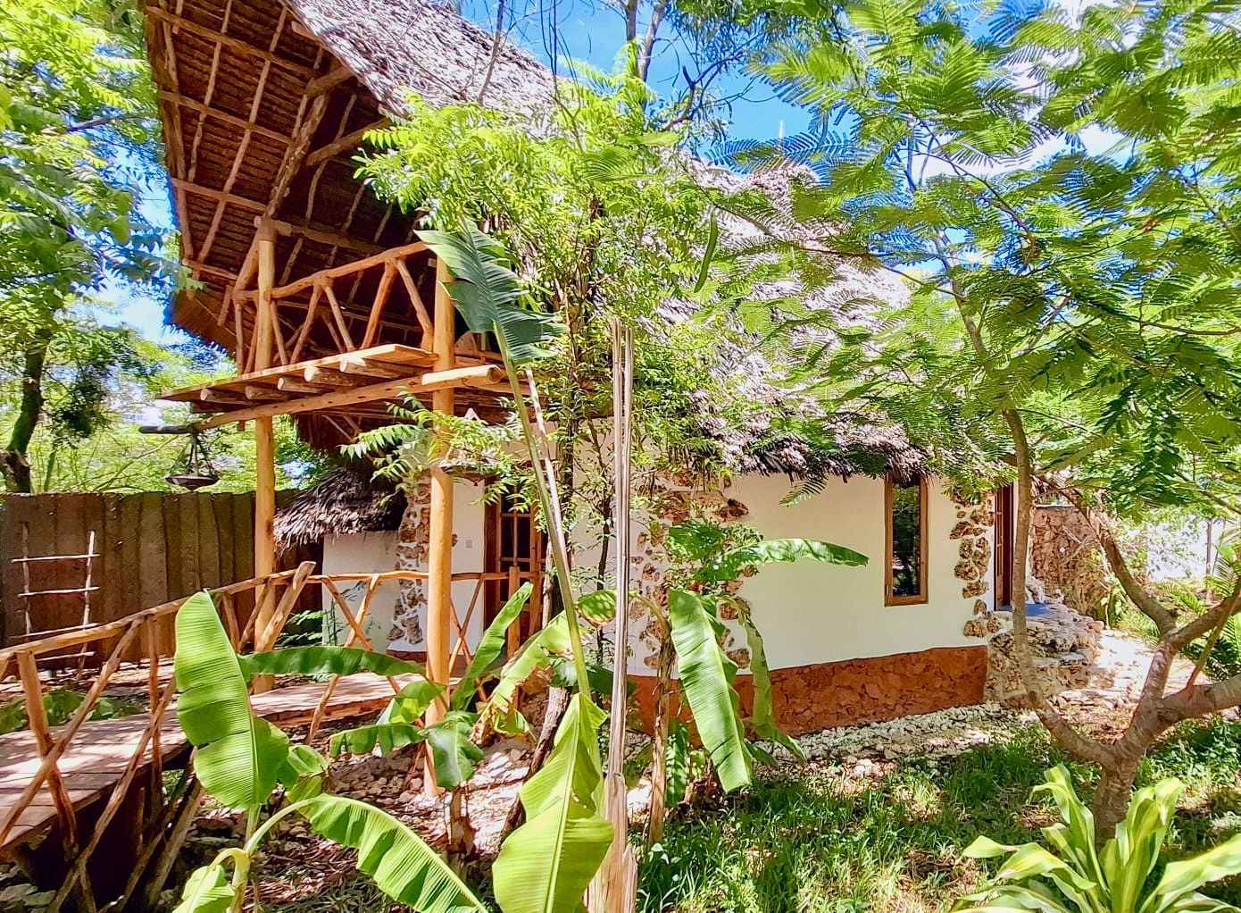 Tropical hut with wooden frame, thatched roof, and lush vegetation.