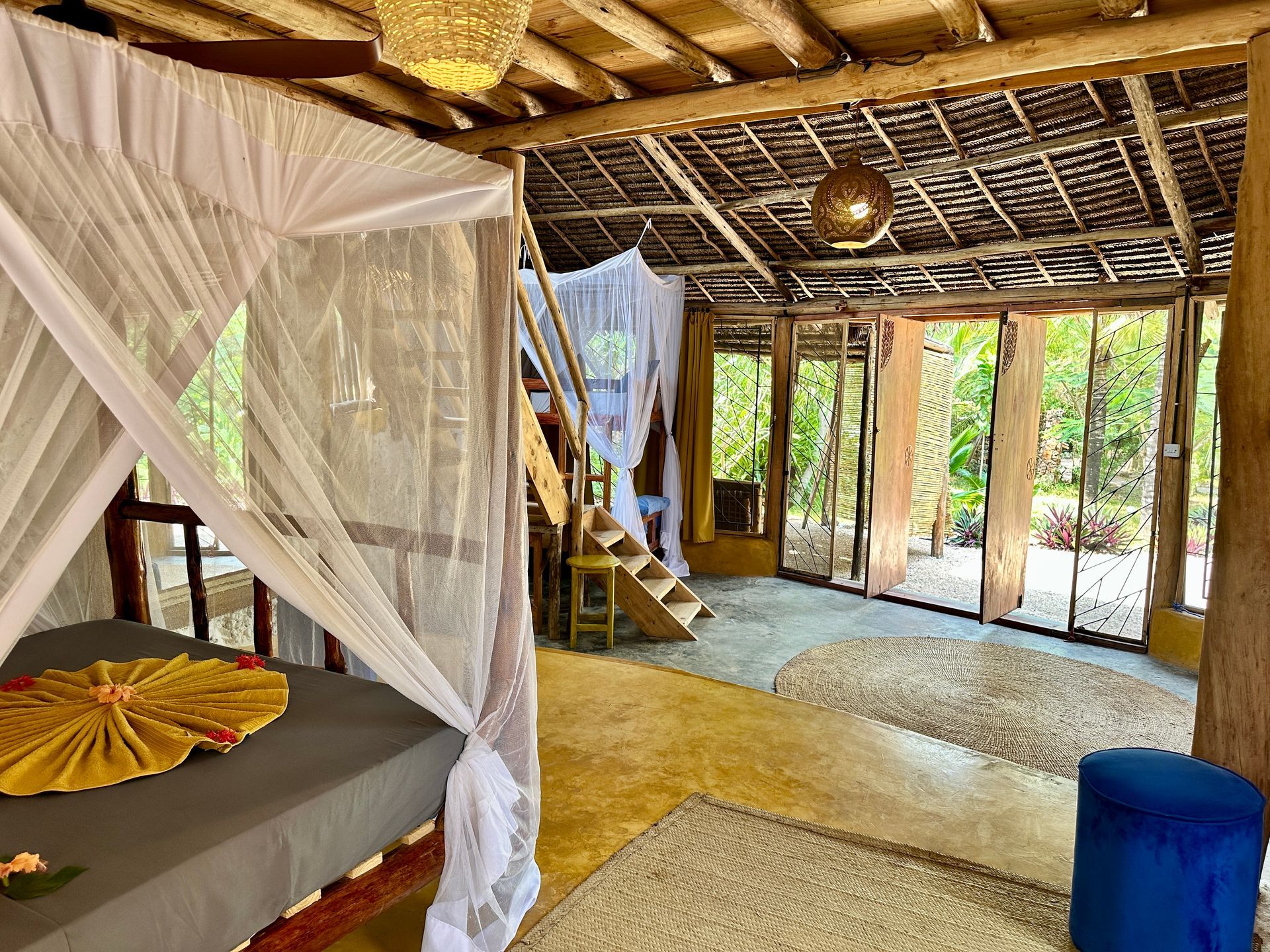 Rustic bedroom with canopy bed, stairs, and open view of greenery.