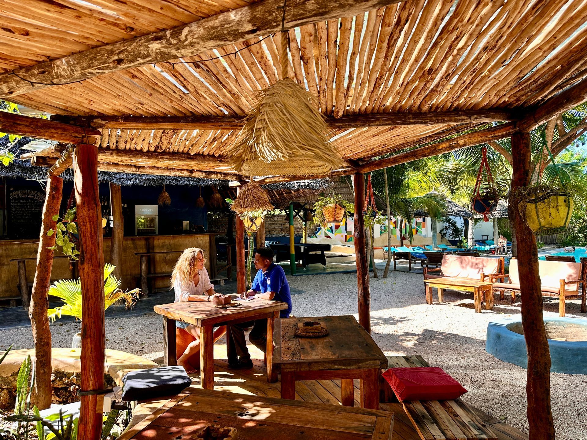 A man and a woman are sitting at a table under a wooden canopy.