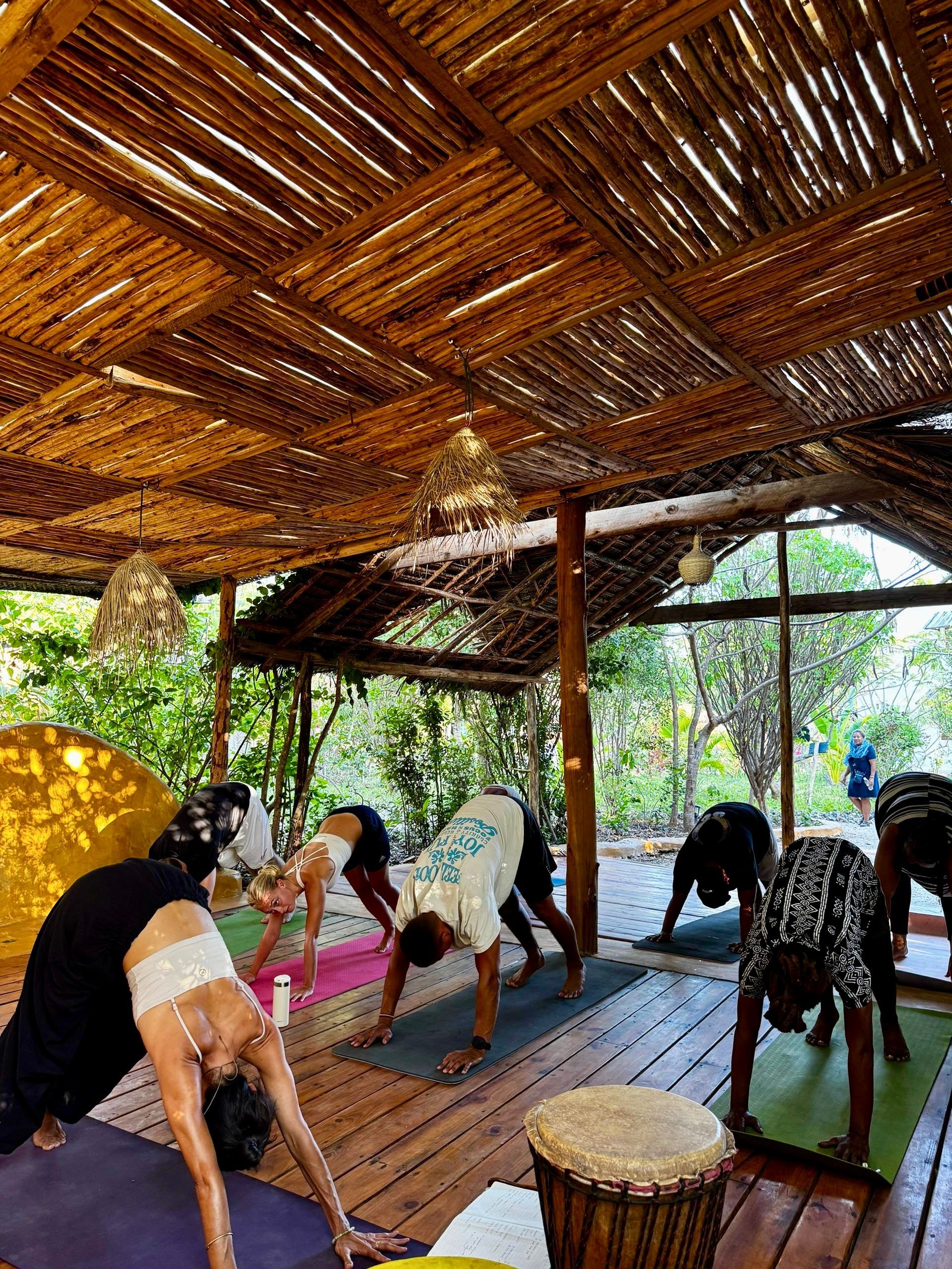 A pool table is sitting under a thatched roof next to a pool.