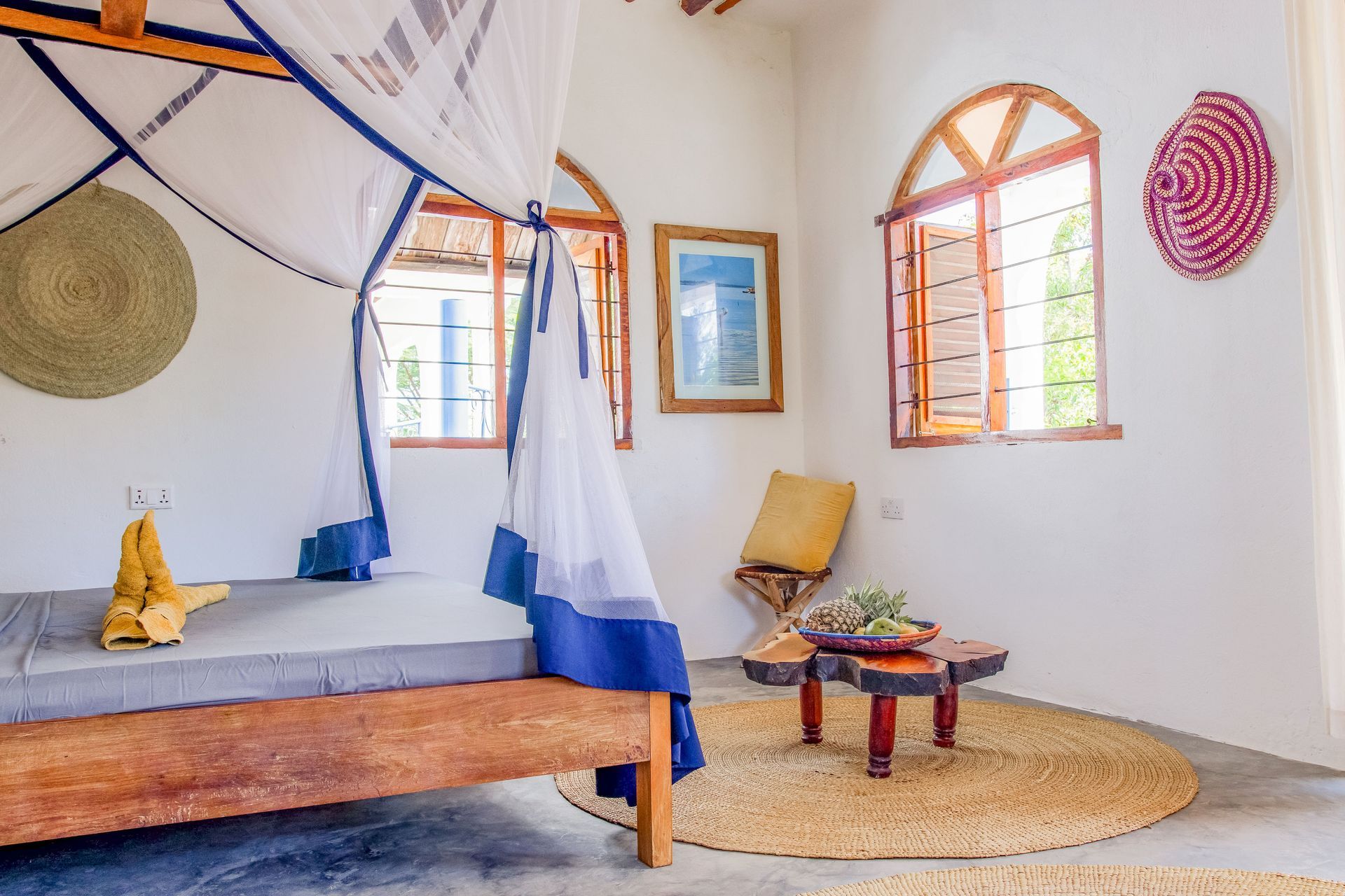 Bedroom with bed, mosquito net, windows, artwork, and a small table.
