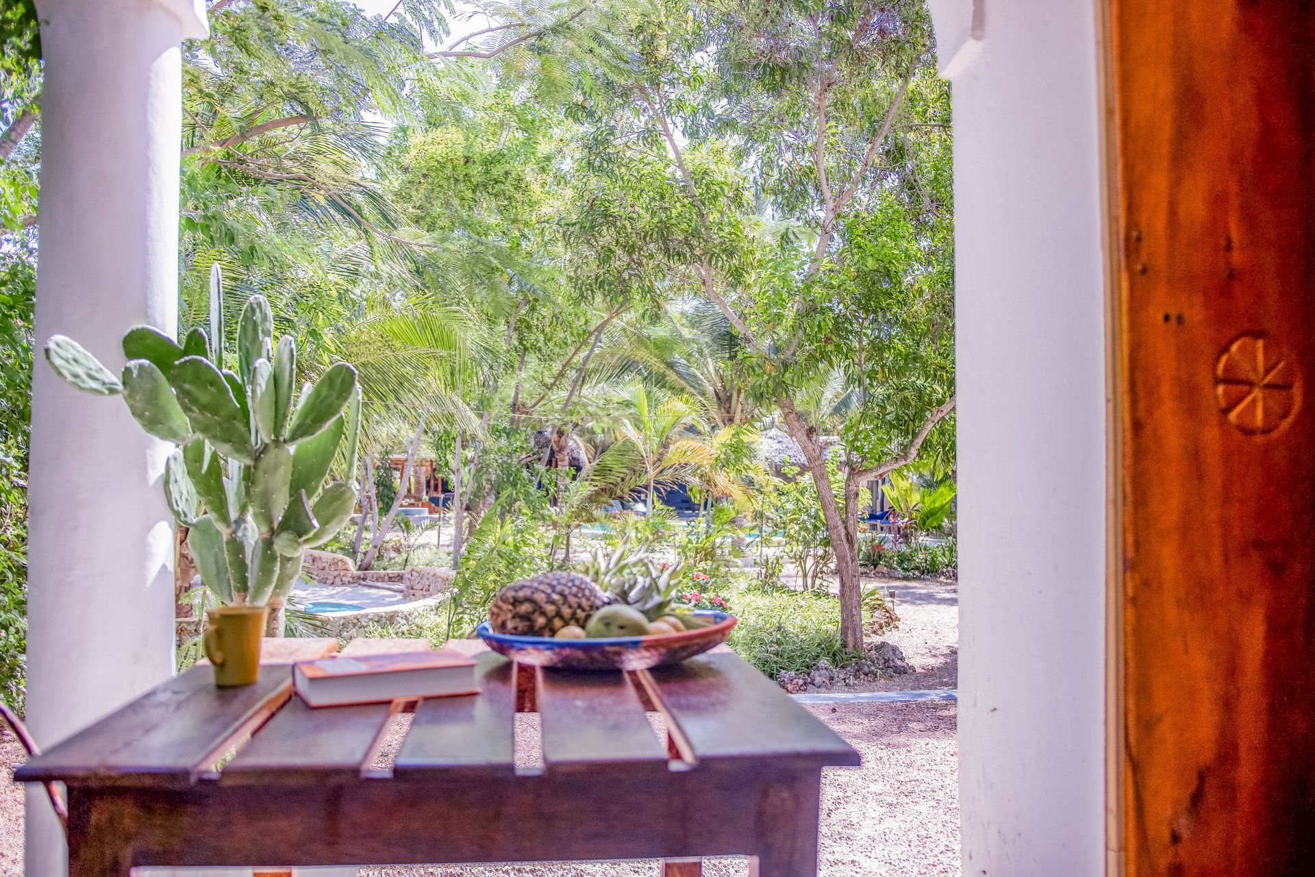 Wooden table with fruit and a cactus on a porch, overlooking a lush green garden.
