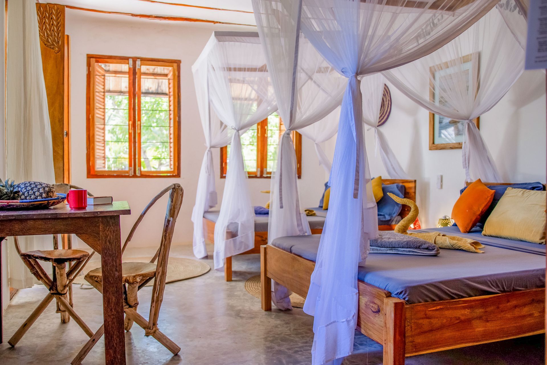 Bedroom with two beds, draped mosquito nets, wooden furniture, and natural light.