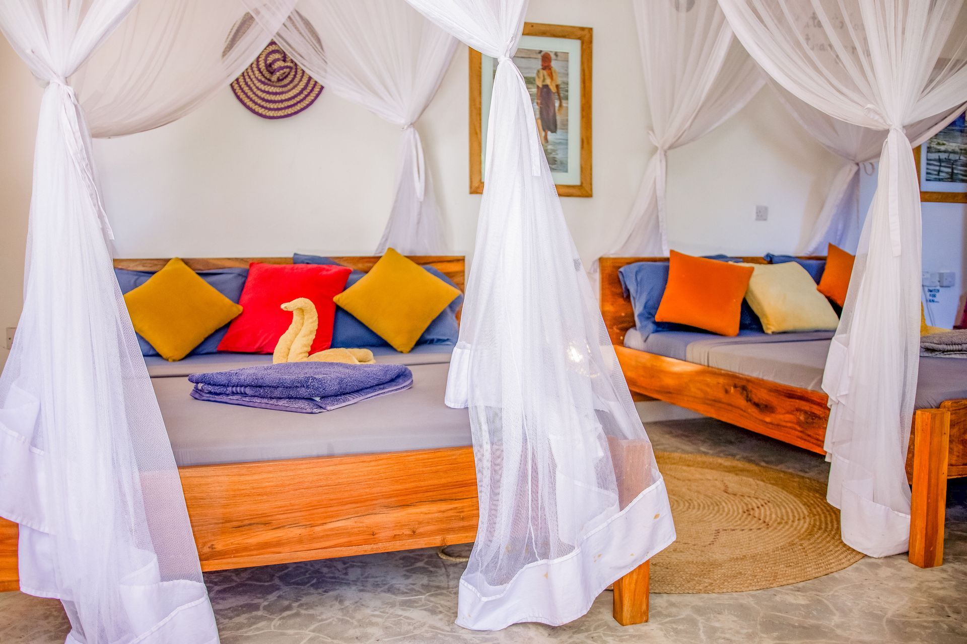 Day beds with canopy netting, colorful pillows, and wall art in a bright, tropical setting.