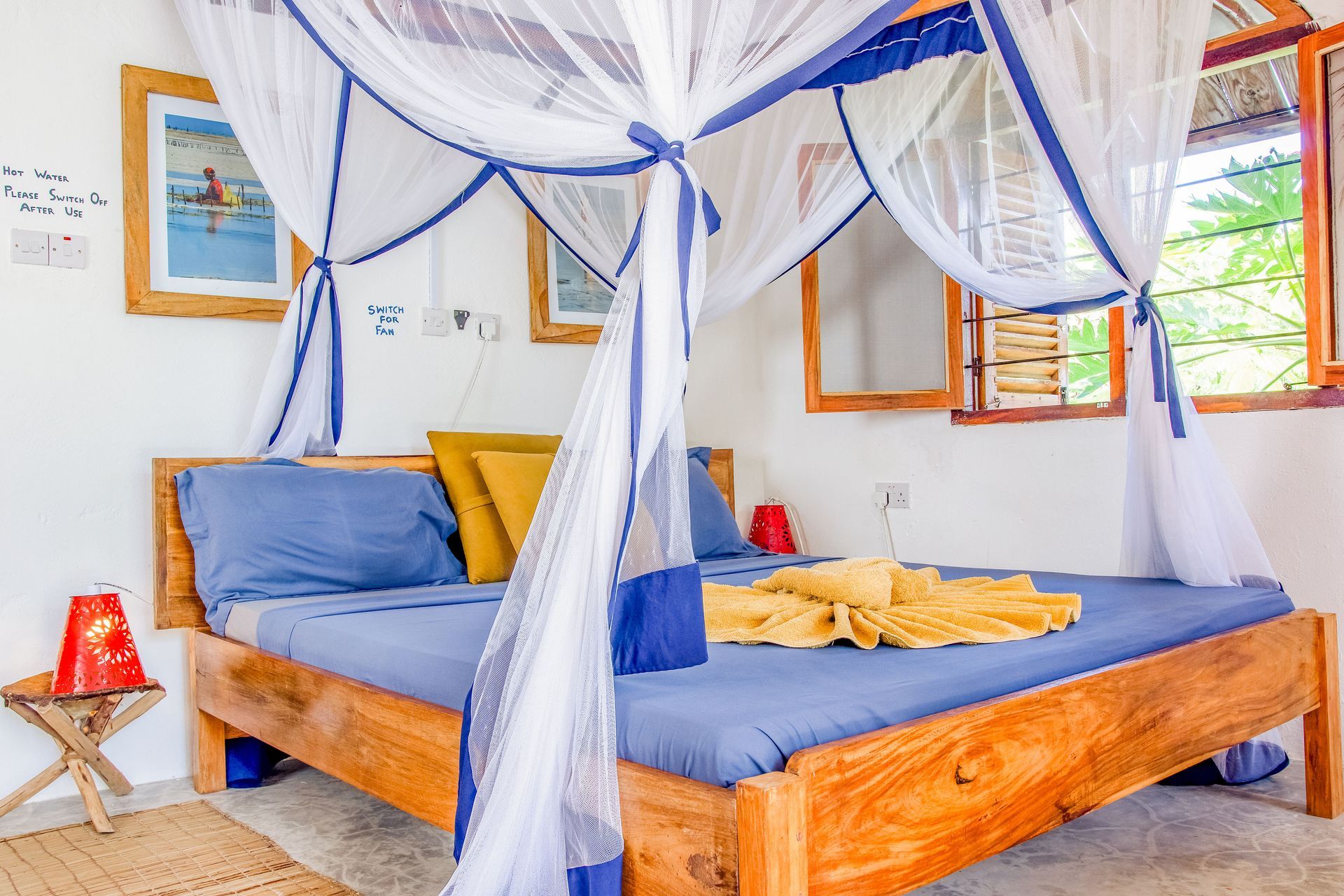 Bedroom with blue bedding, mosquito net, wooden bed frame, and art on the wall.