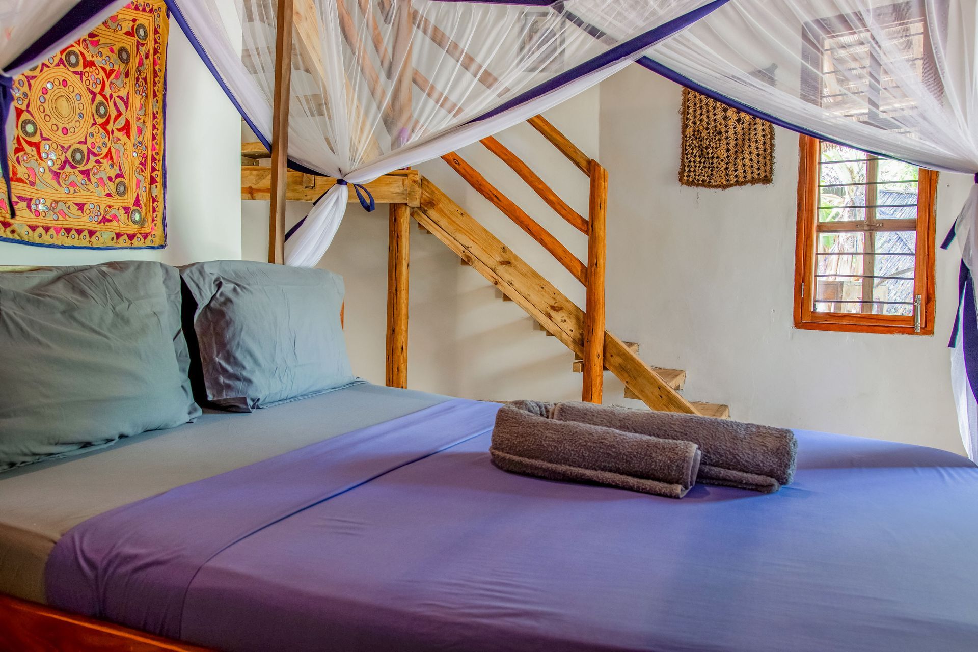 Bedroom with a bed, stairs, and decorative items; purple sheets, gray pillows.