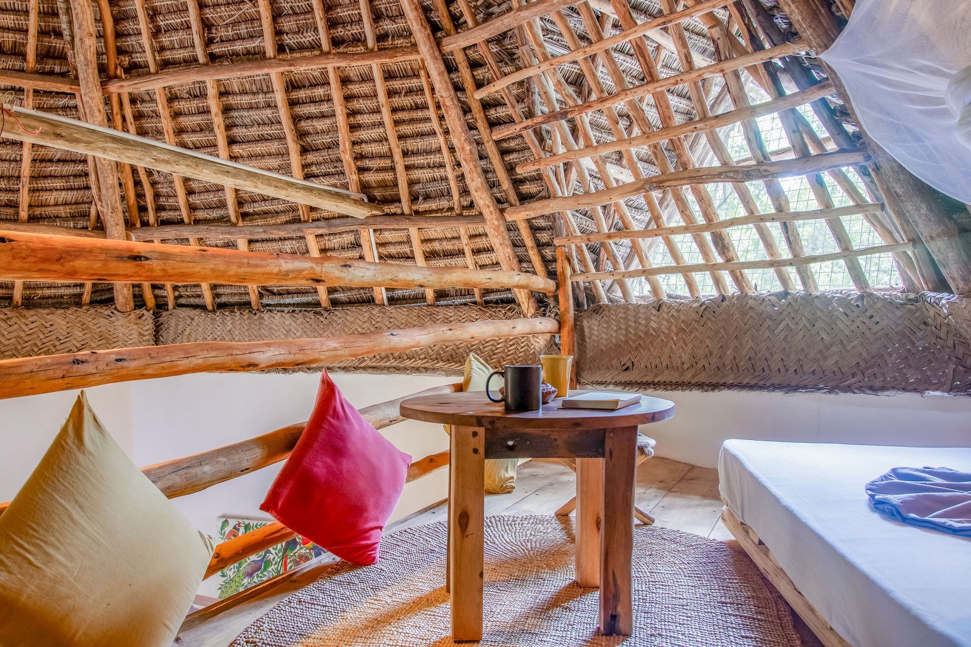 Cozy room with thatched roof, round table, bed, and pillows.