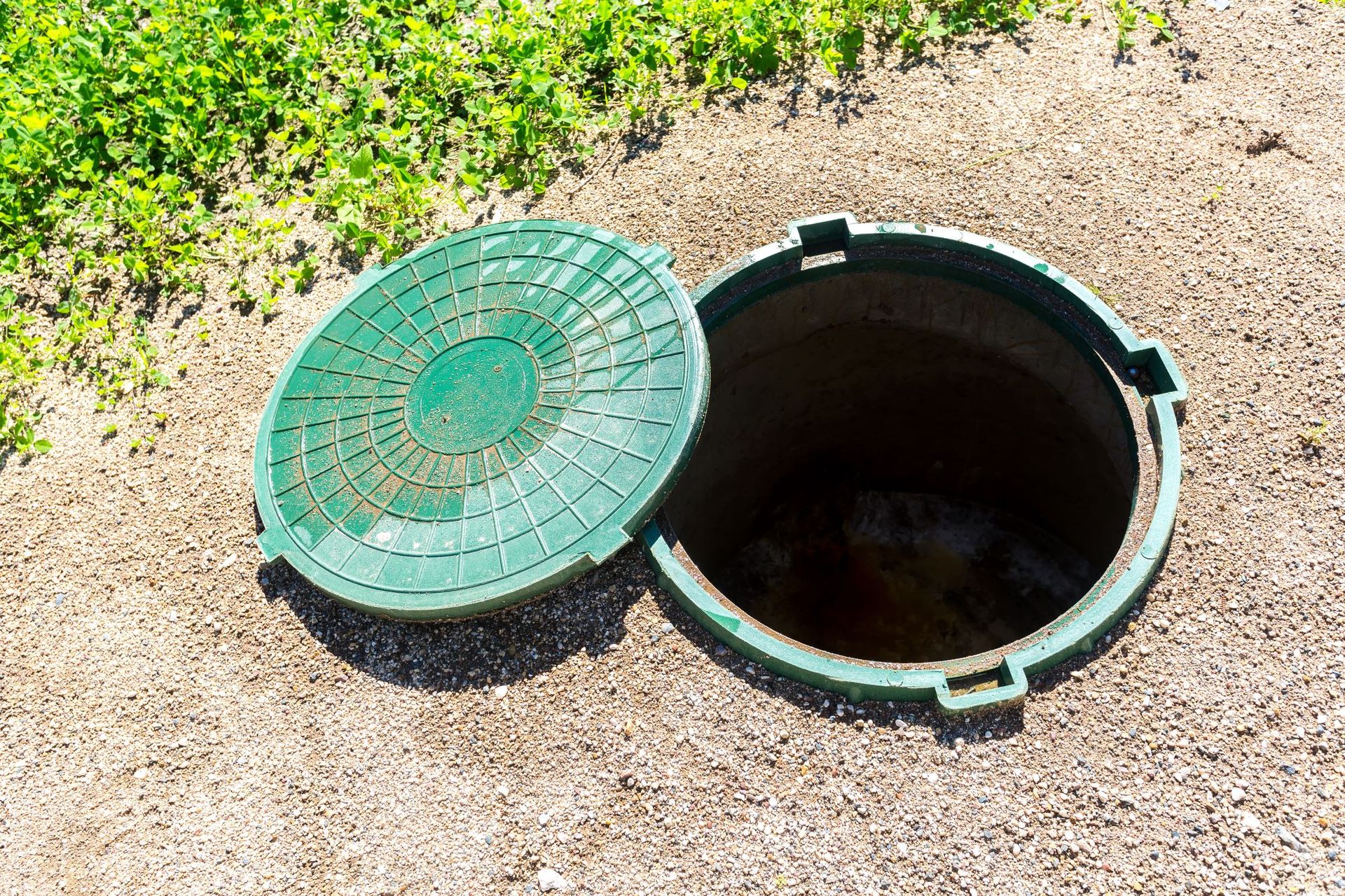 A green manhole cover is open and sitting on the ground.