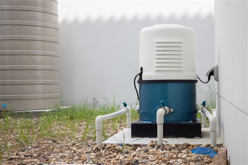 A water pump is sitting outside of a building next to a water tank.