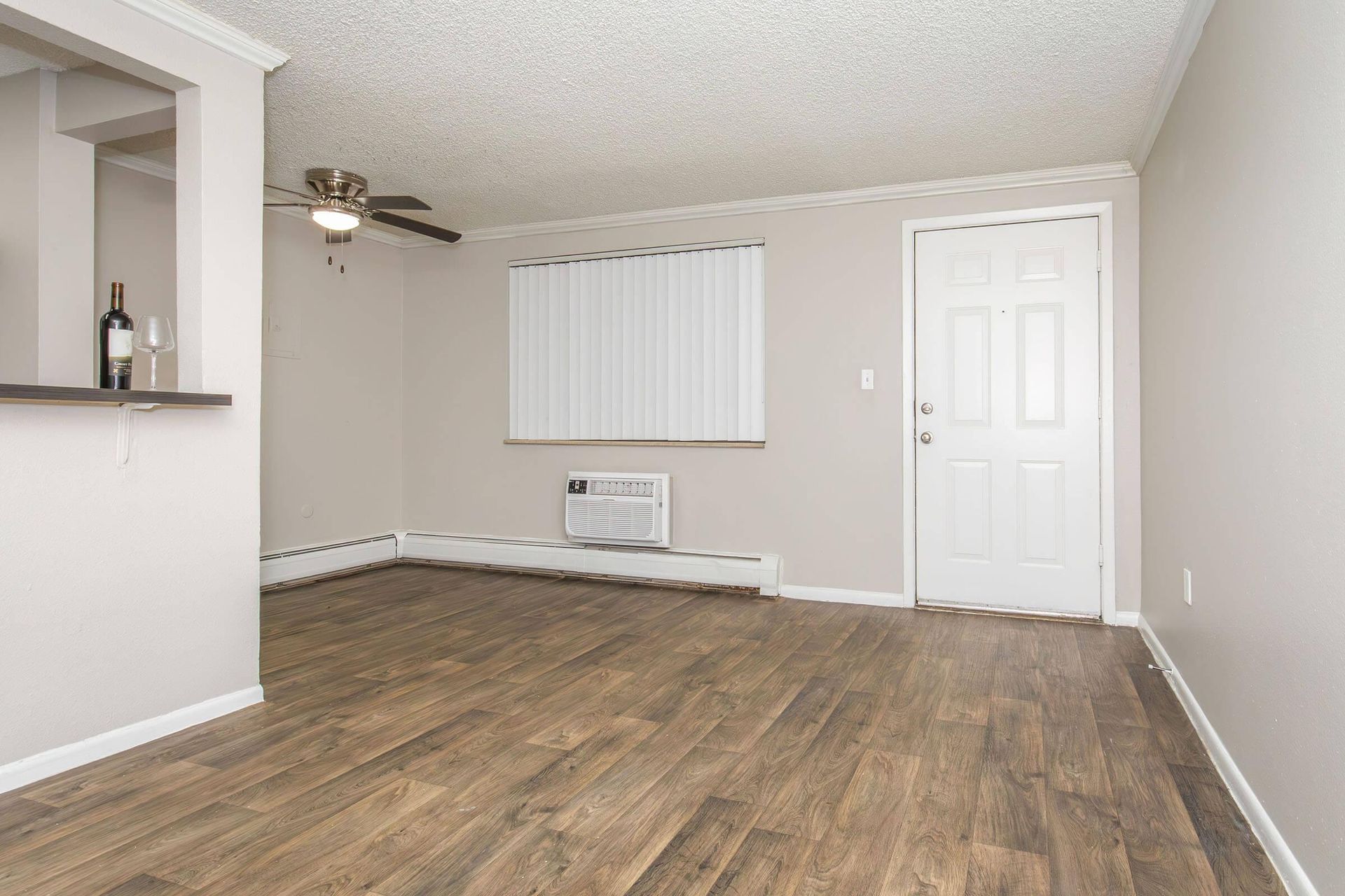 Empty apartment living room with wood-look floor, window with blinds, and a white door.