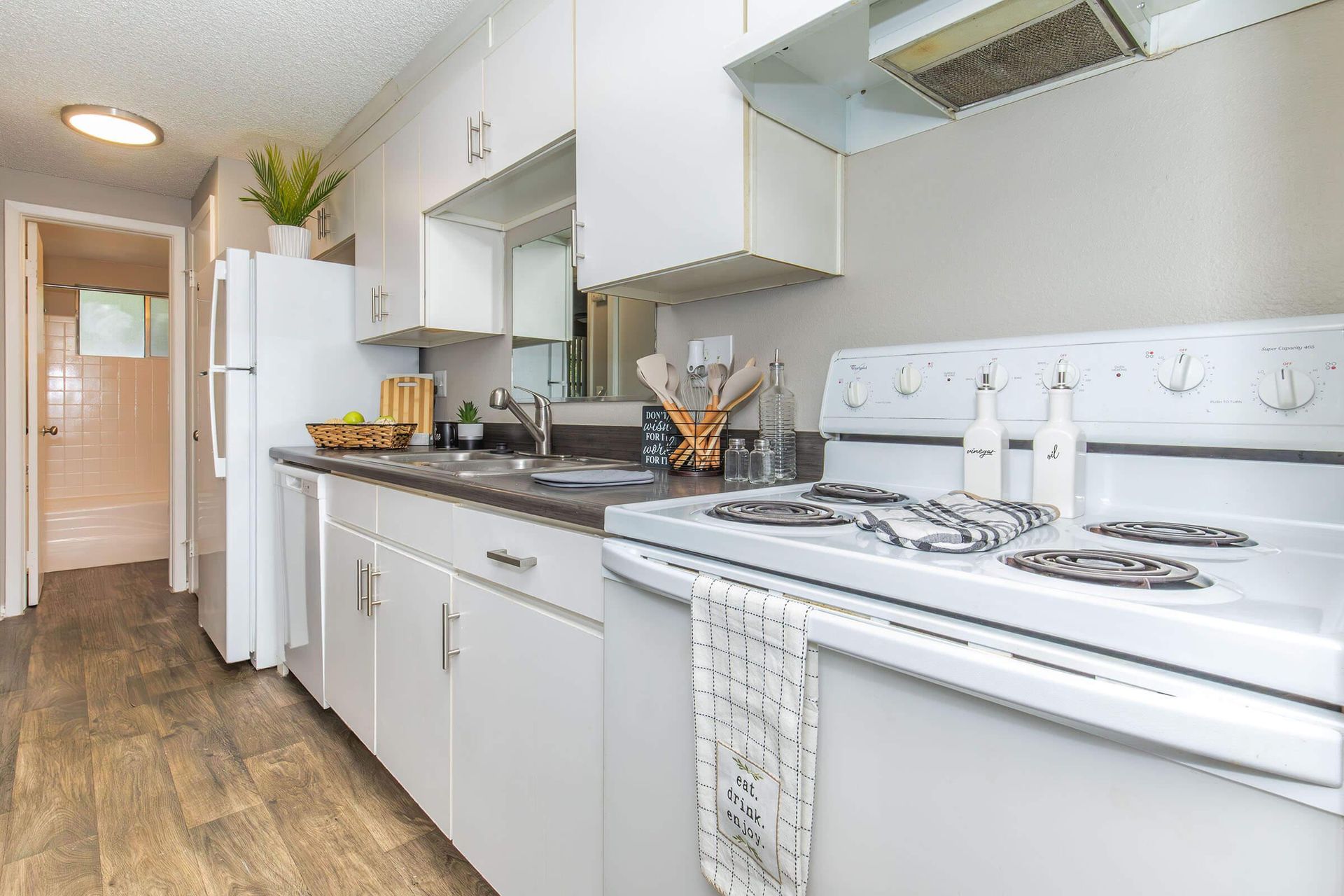 White kitchen with stove, cabinets, and appliances; light gray walls; wood-look floor.