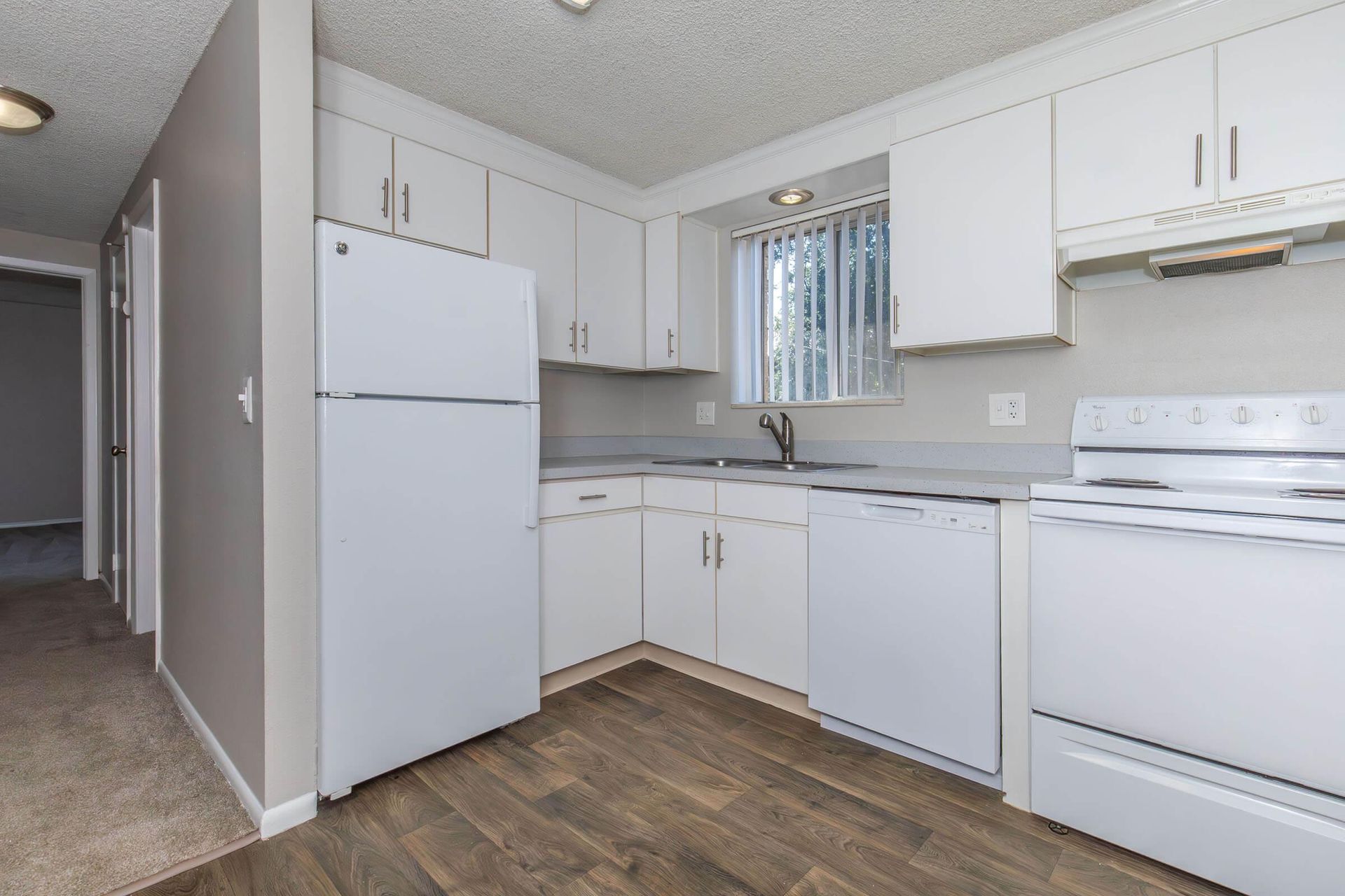 White kitchen with cabinets, appliances, and gray countertops. Dark wood-look flooring.