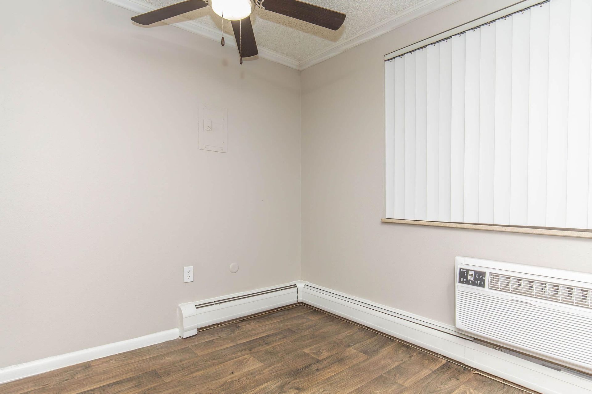 Empty room with wood-look floor, tan walls, ceiling fan, window with blinds, and heater.