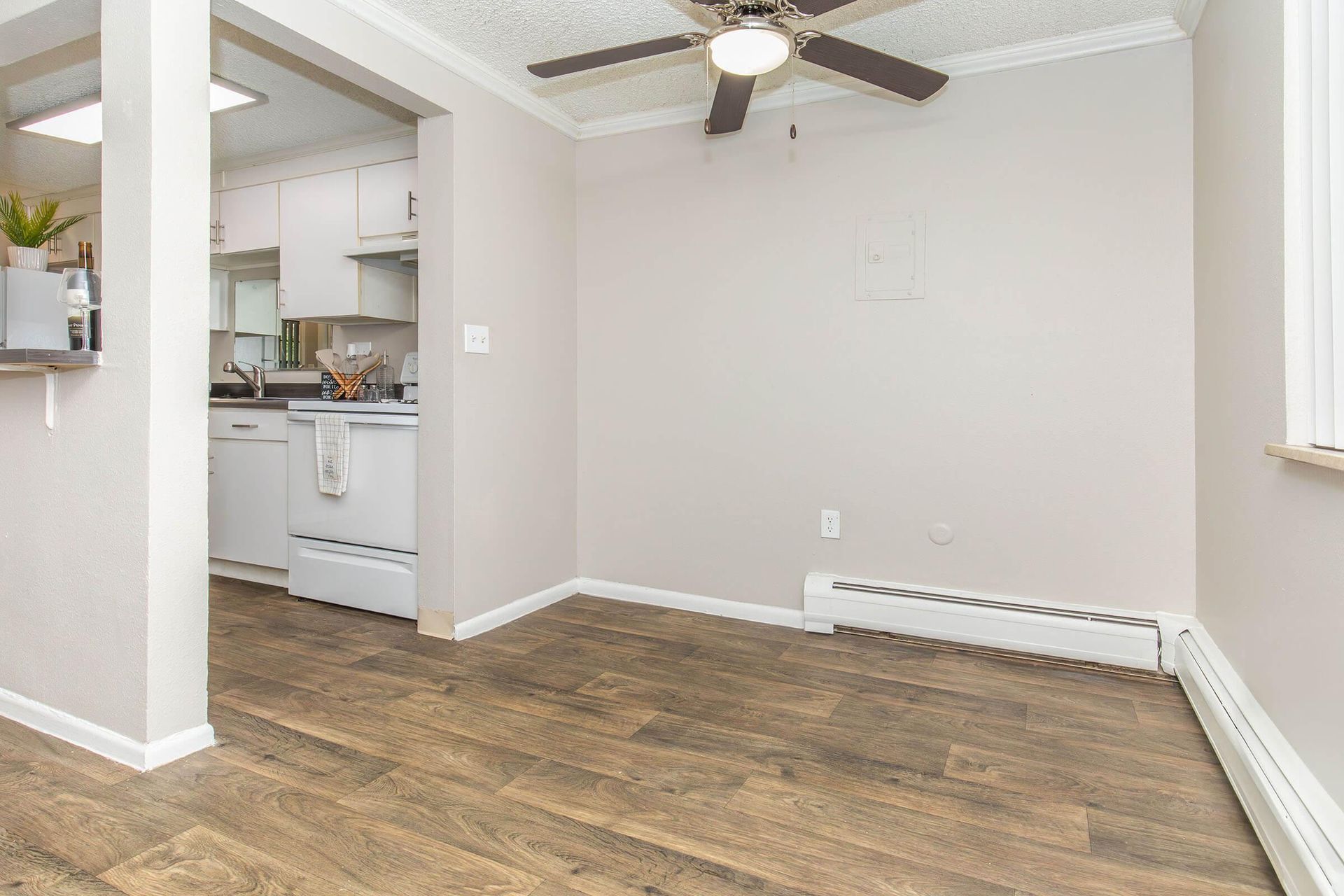 Empty dining area with wooden floor, beige walls, and a view of the kitchen.