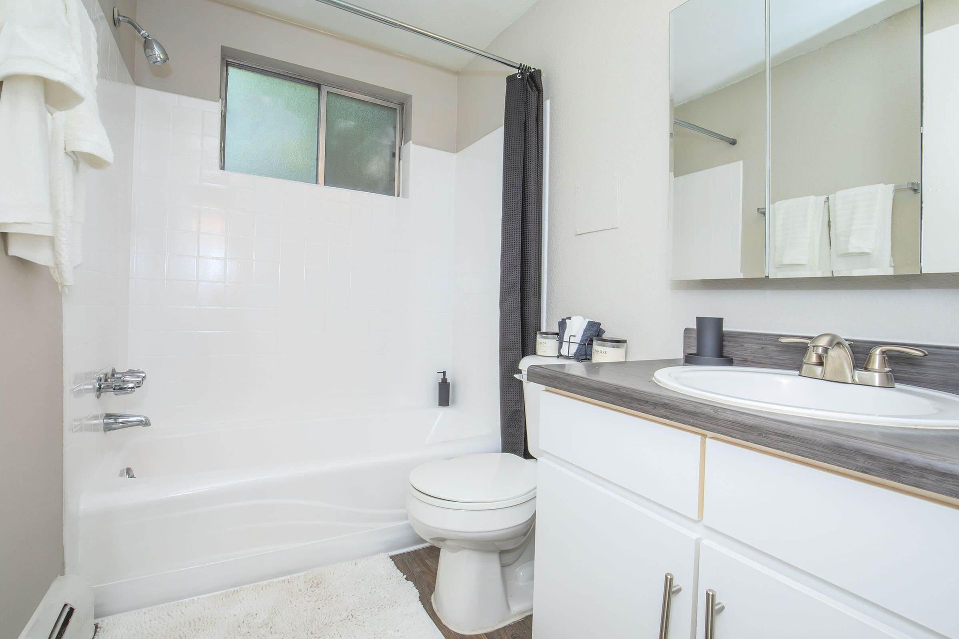 White bathroom with a tub, toilet, vanity, and small window.