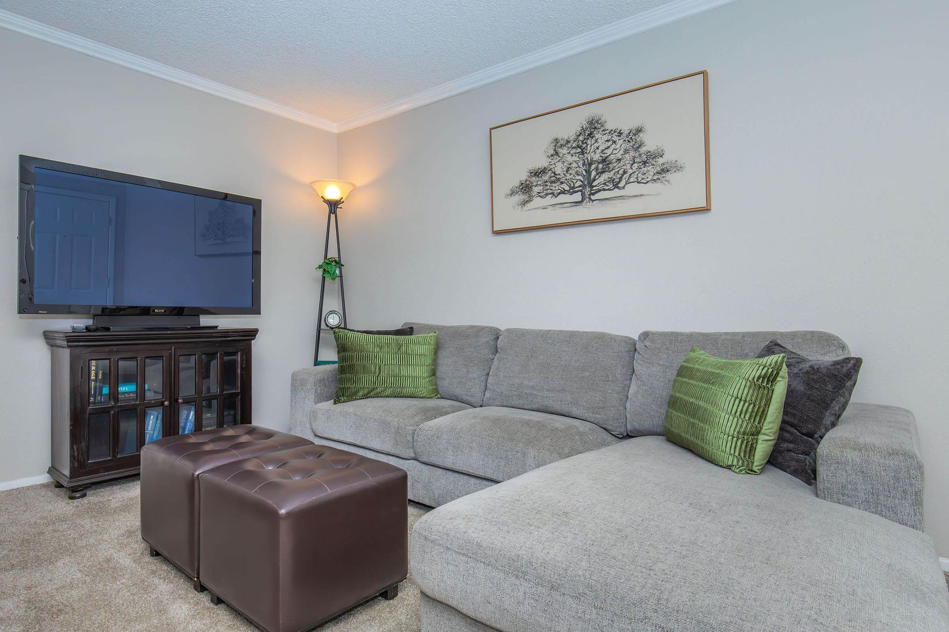 Cozy living room with gray sectional sofa, TV, ottoman, and artwork.