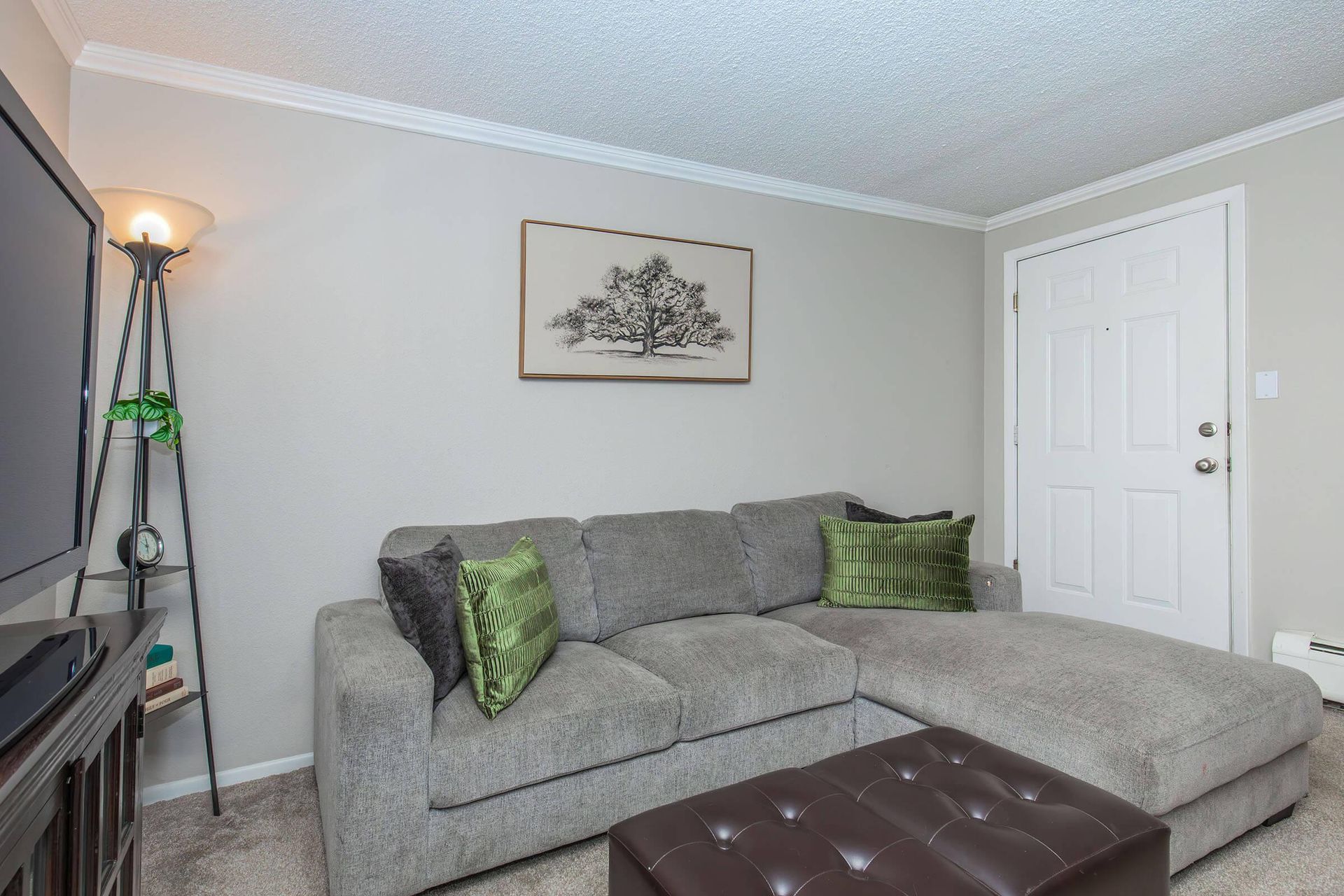 Gray sectional sofa in a living room with green pillows, a leather ottoman, and artwork.