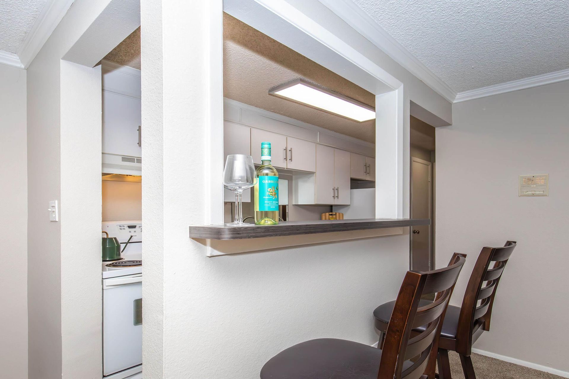 A partial view of a kitchen with a bar, two stools, and a bottle of liquor.