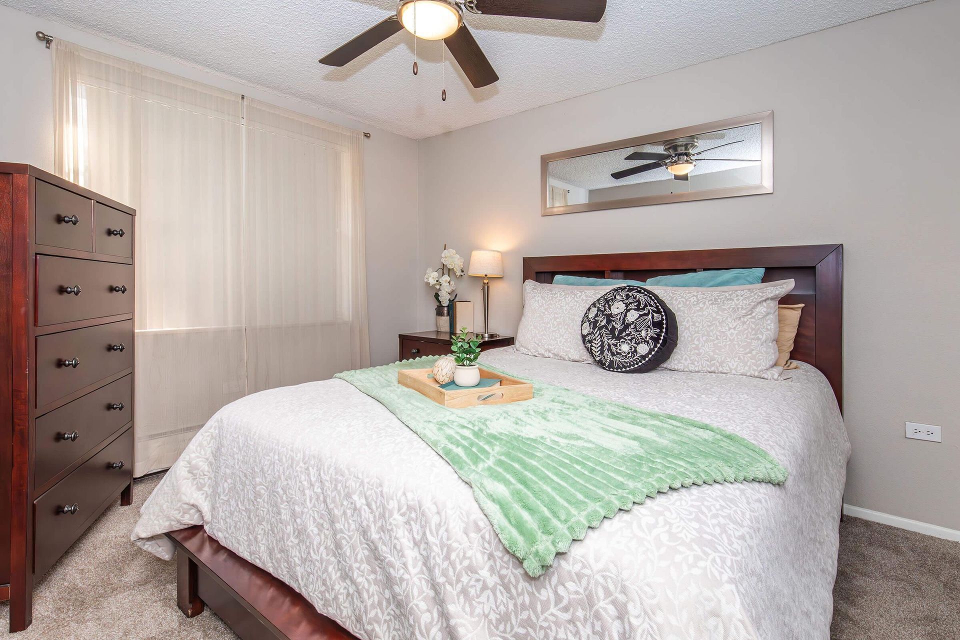 Bedroom with a dark wooden bed, dresser, and neutral walls. A green blanket rests on the bed.