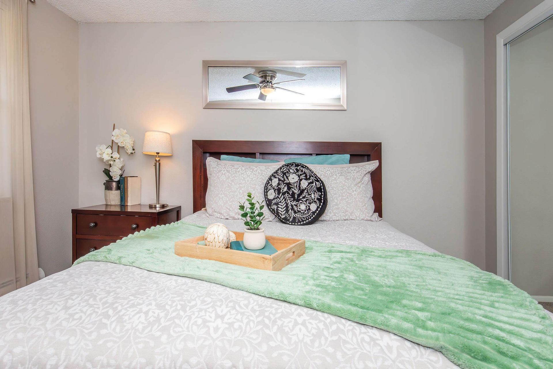 Bedroom with bed, nightstand, and decorations; green blanket, neutral walls.