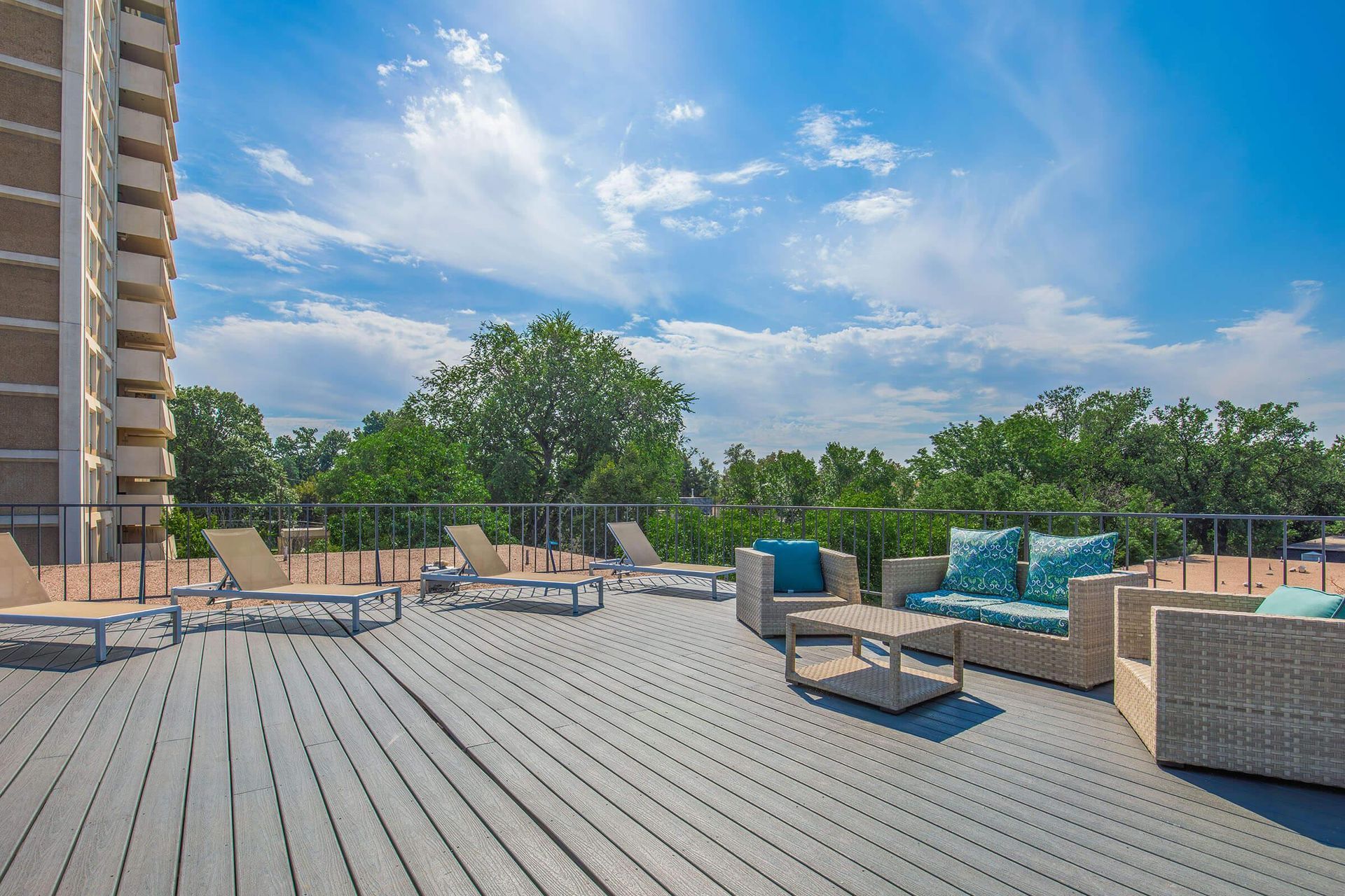 Rooftop patio with seating, lounge chairs, and wooden deck. Blue sky and trees in background.