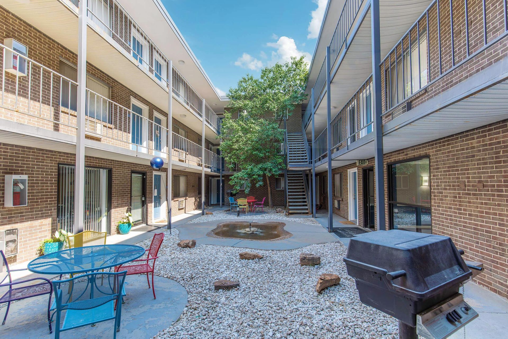 Courtyard of a brick apartment building with seating, grill, and central tree.