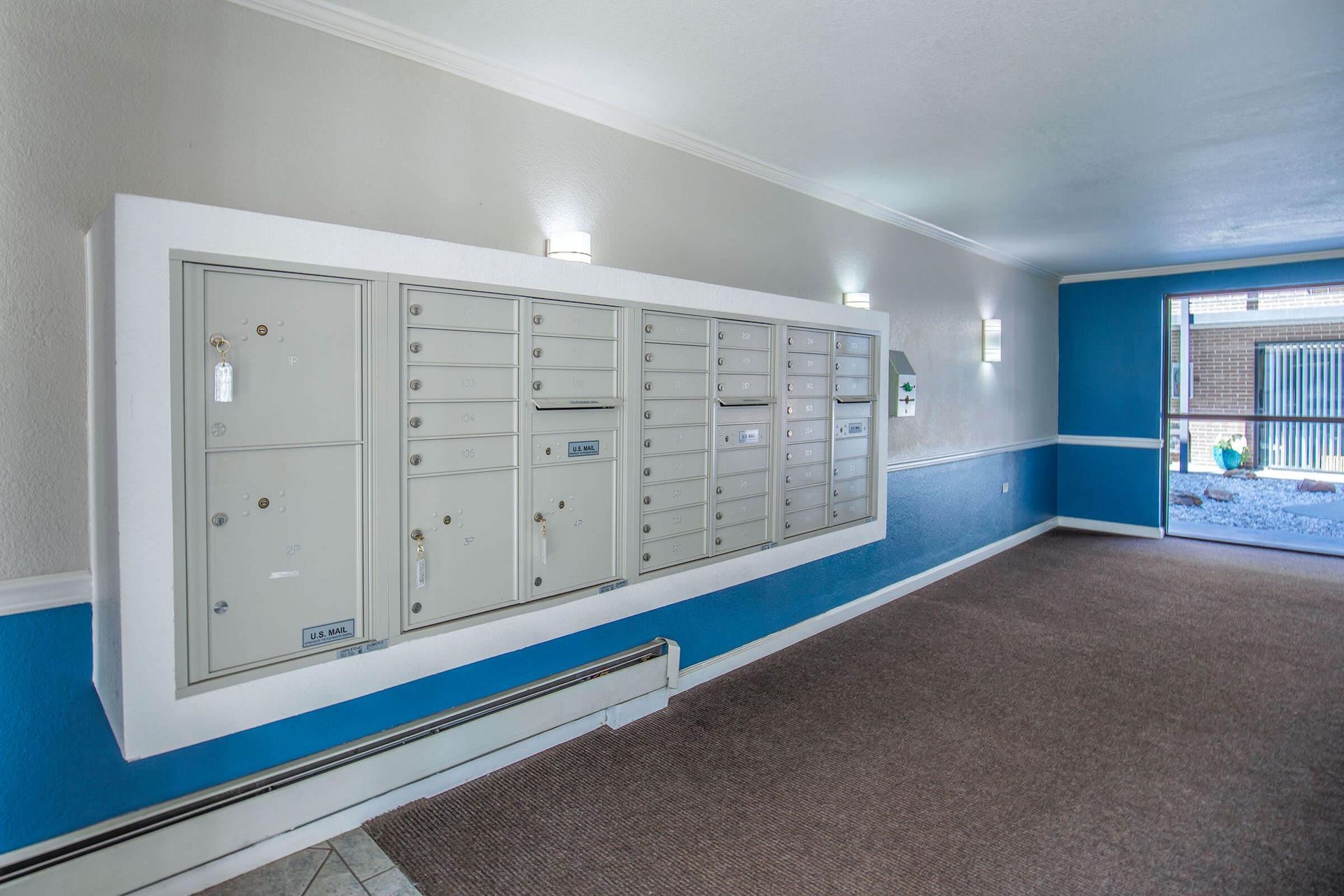 Apartment lobby with a wall of mailboxes, blue and white paint, and brown carpet.
