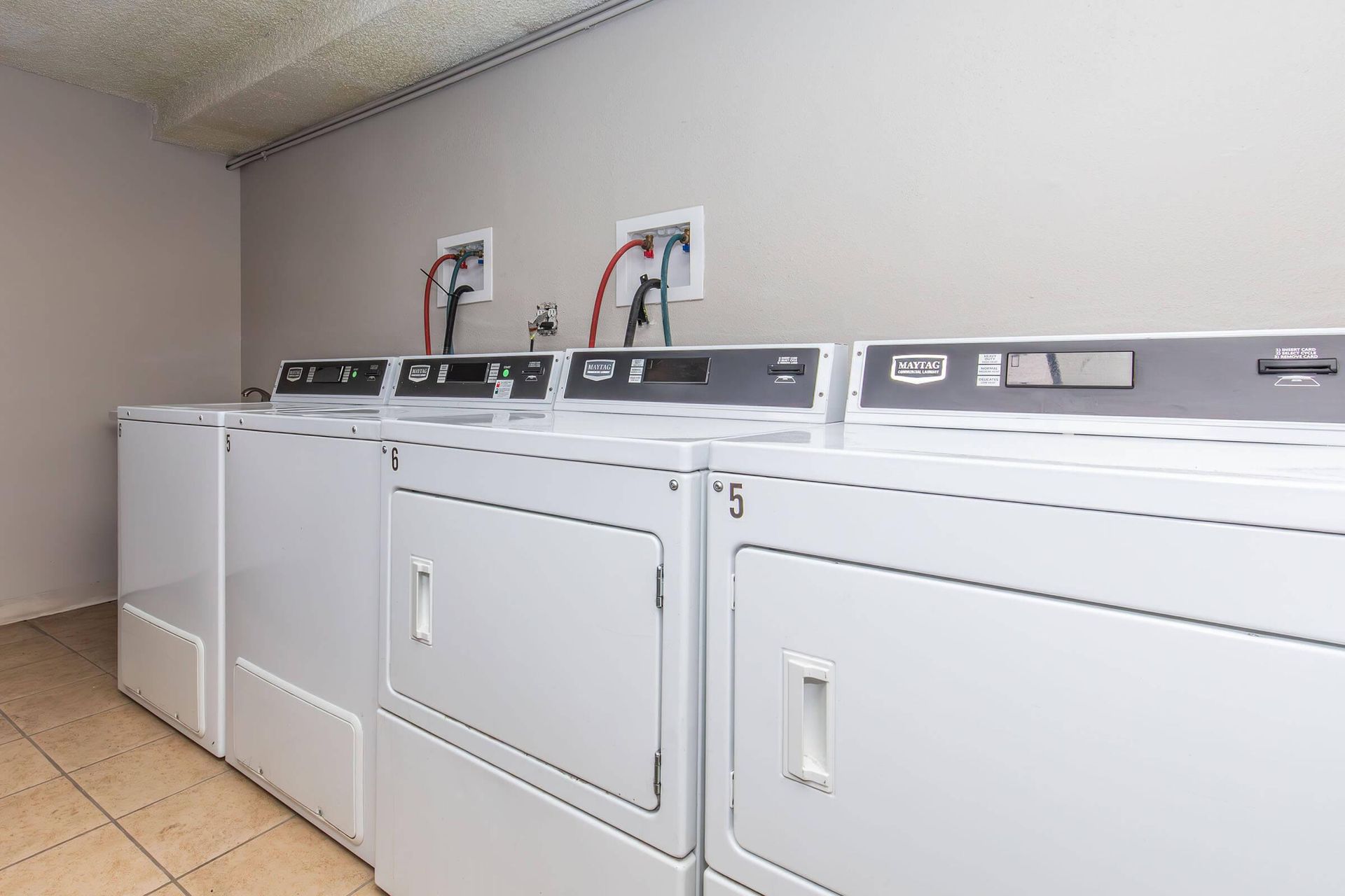 Row of white laundry dryers in a neutral-colored room, near electrical outlets.