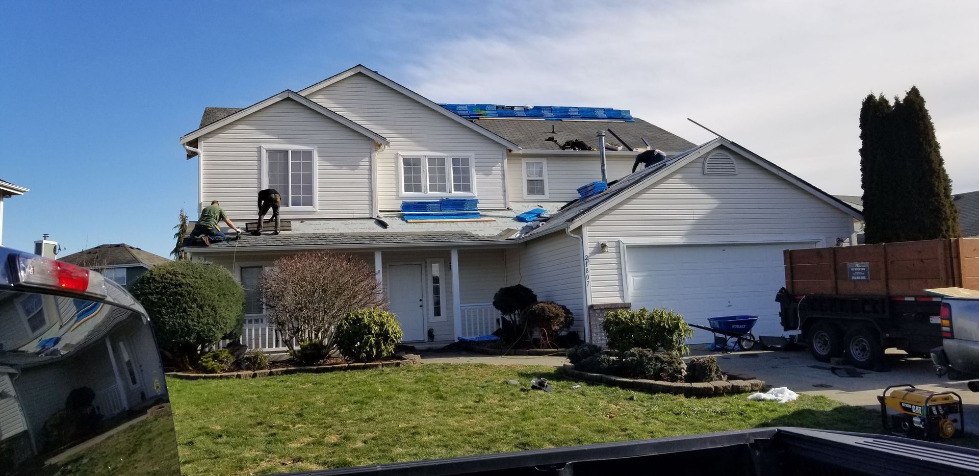 Worker on a rooftop beside gray shingles and white roof under clear sky.