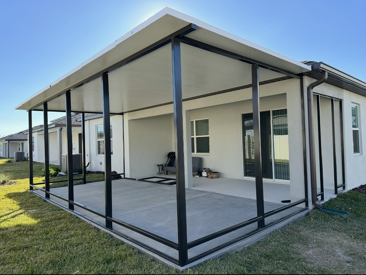 Pool covered by clear, segmented structure. White lounge chairs sit inside, trees in background. Cloudy sky.