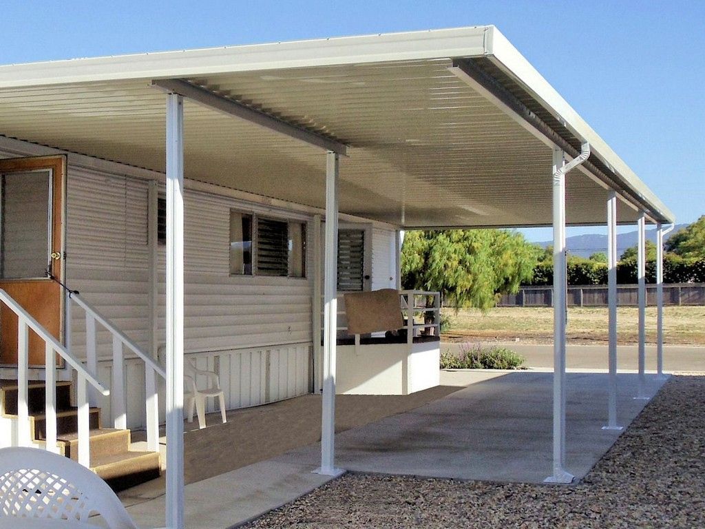Modern house exterior with carport, driveway, and garage. Green plants and stone accents.