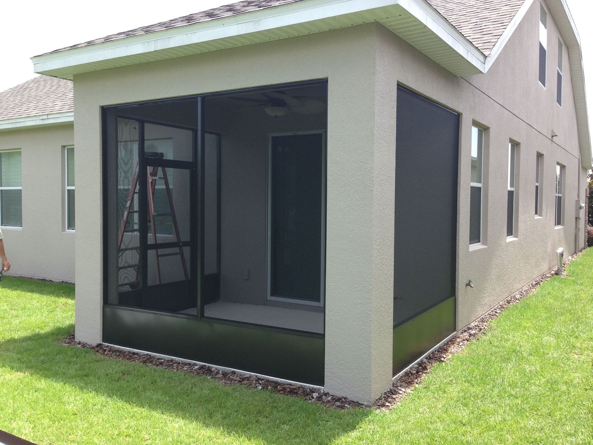 Rooftop terrace with glass-walled sunroom, plants, and a wooden deck, overlooking a city.