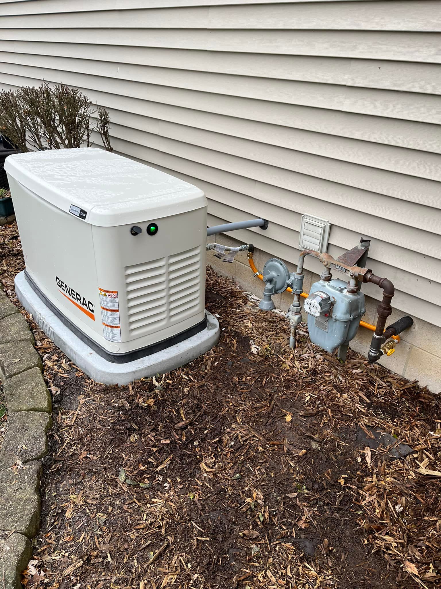 A generator is sitting on the side of a house next to a gas meter.