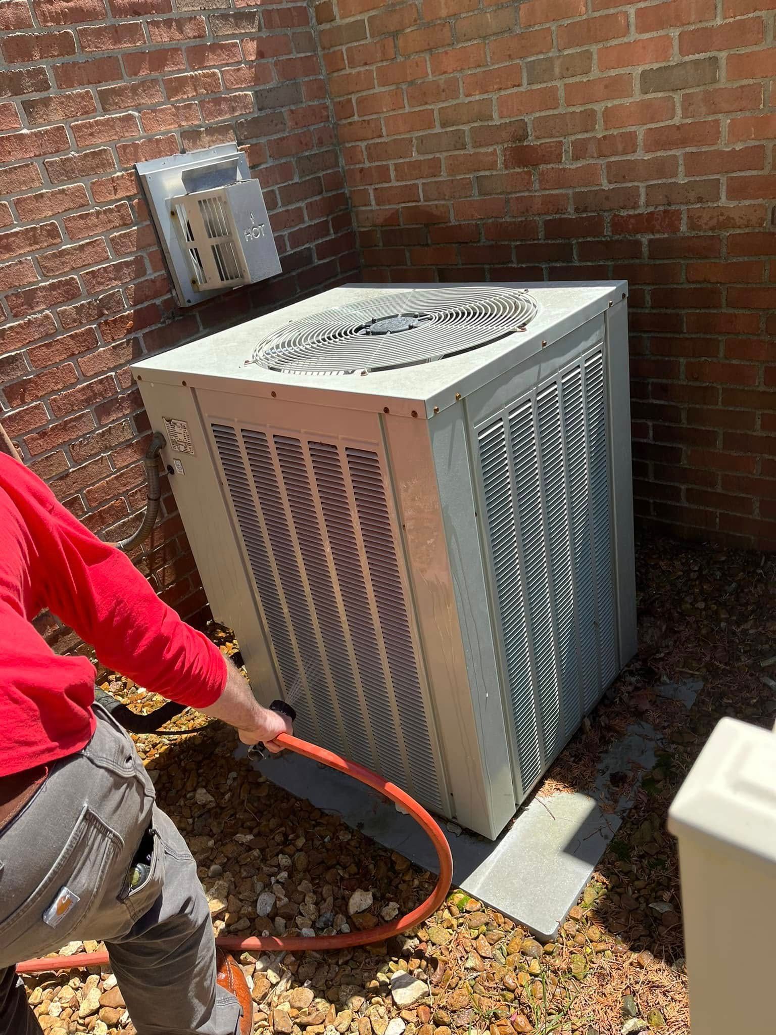 A man is cleaning an air conditioner with a hose.