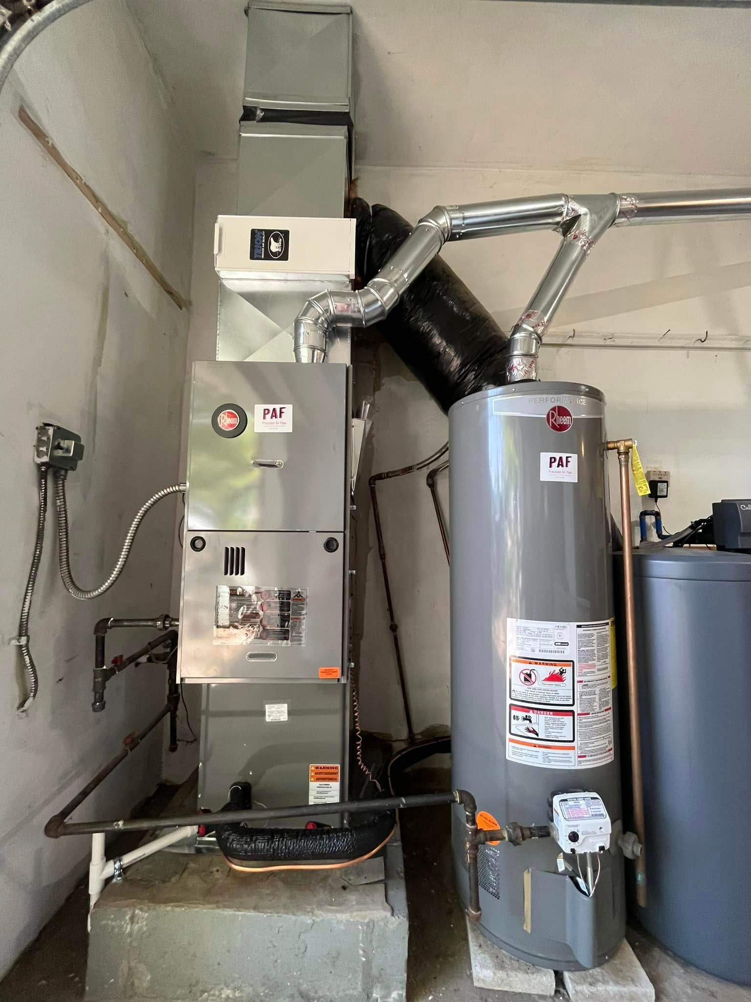 A water heater is sitting next to an air conditioner in a garage.