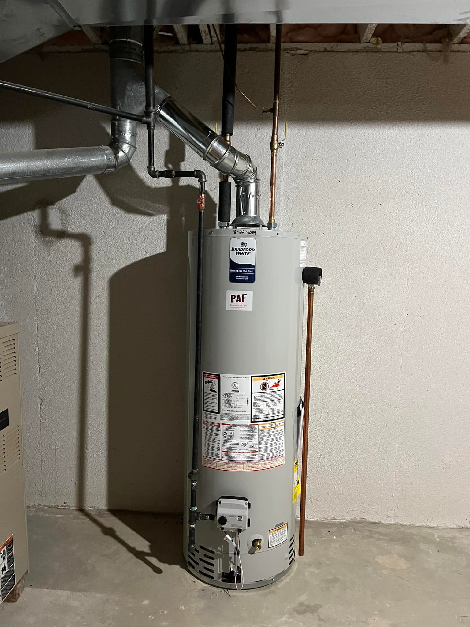 A water heater is sitting in a basement next to a wall.