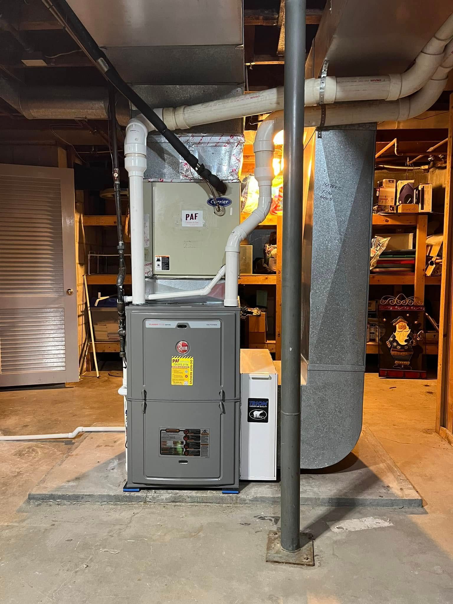 A furnace is sitting in a basement next to a pipe.