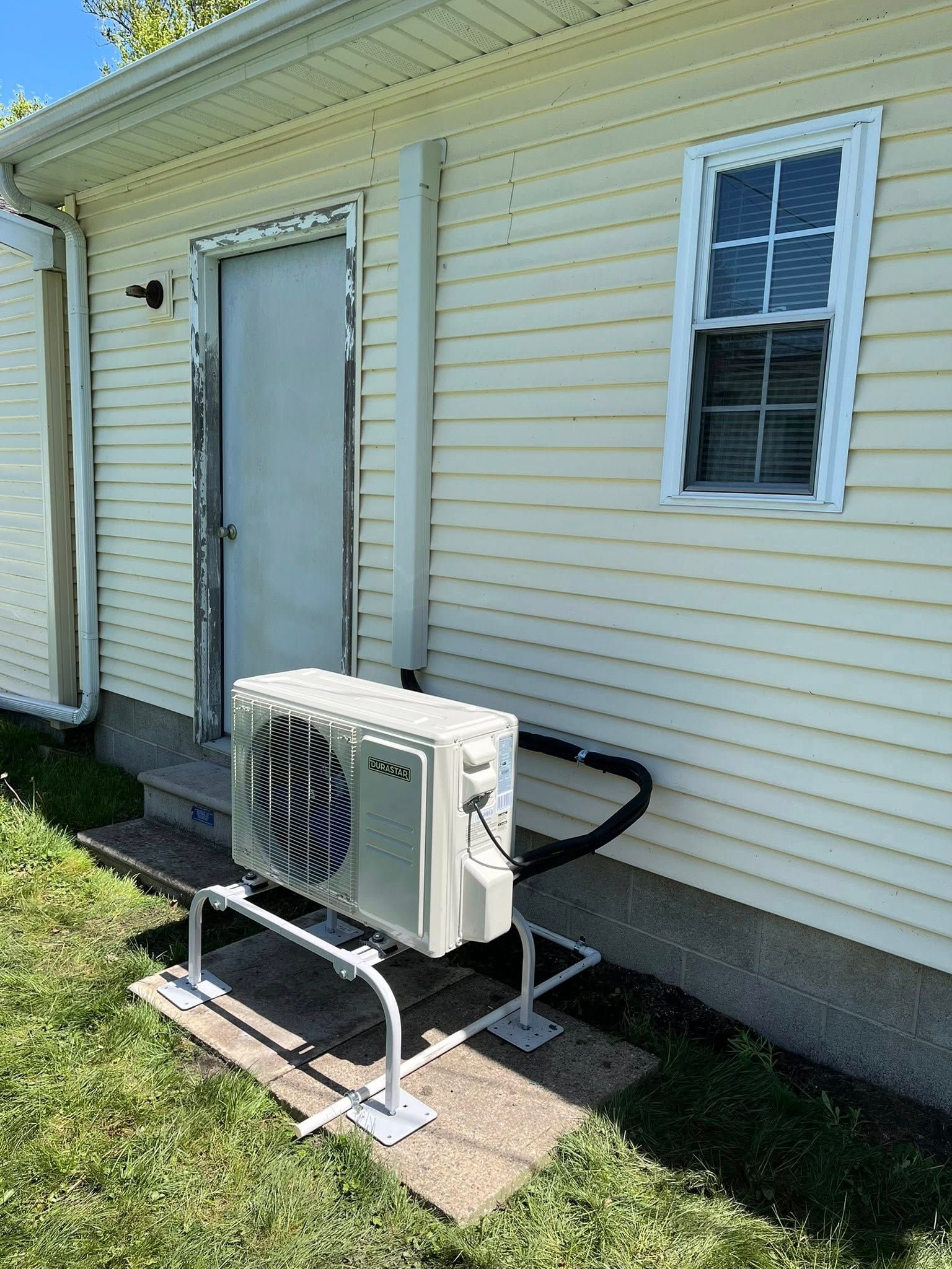 A small air conditioner is sitting on the side of a house.