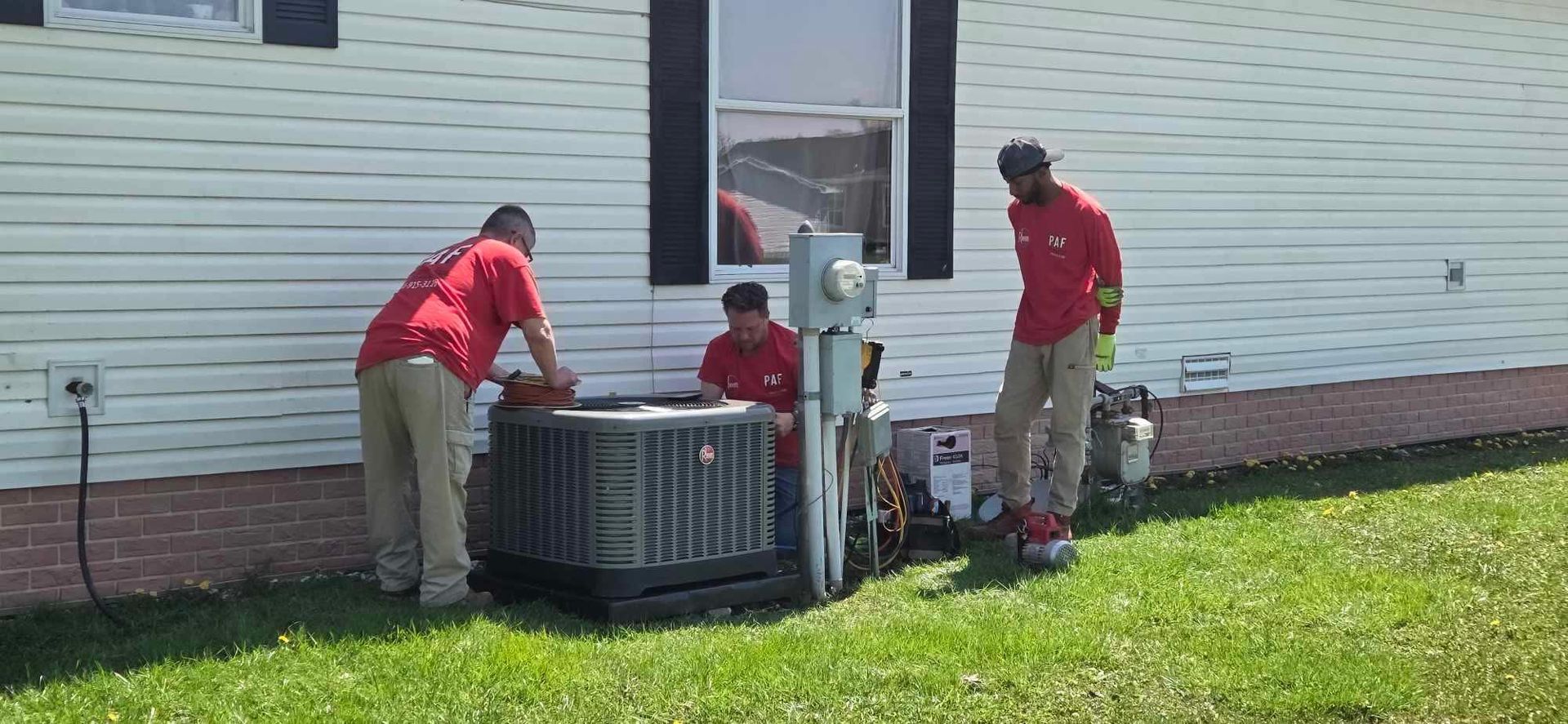 Three men are working on an air conditioner outside of a house.
