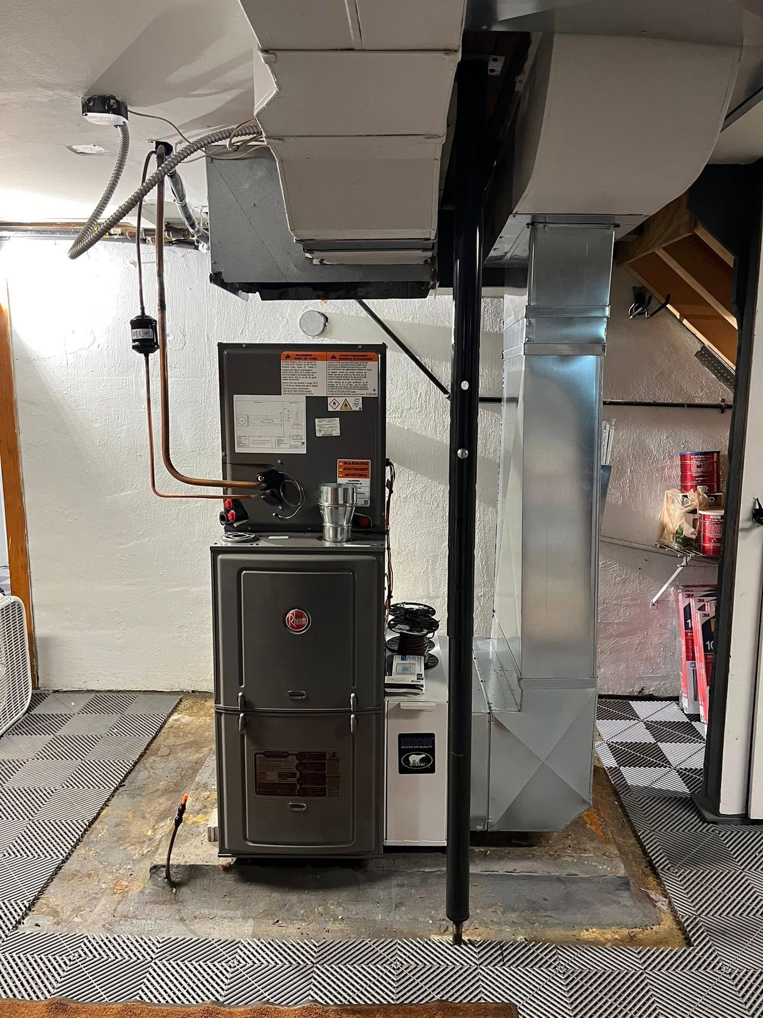 A furnace is sitting in a basement next to a duct.