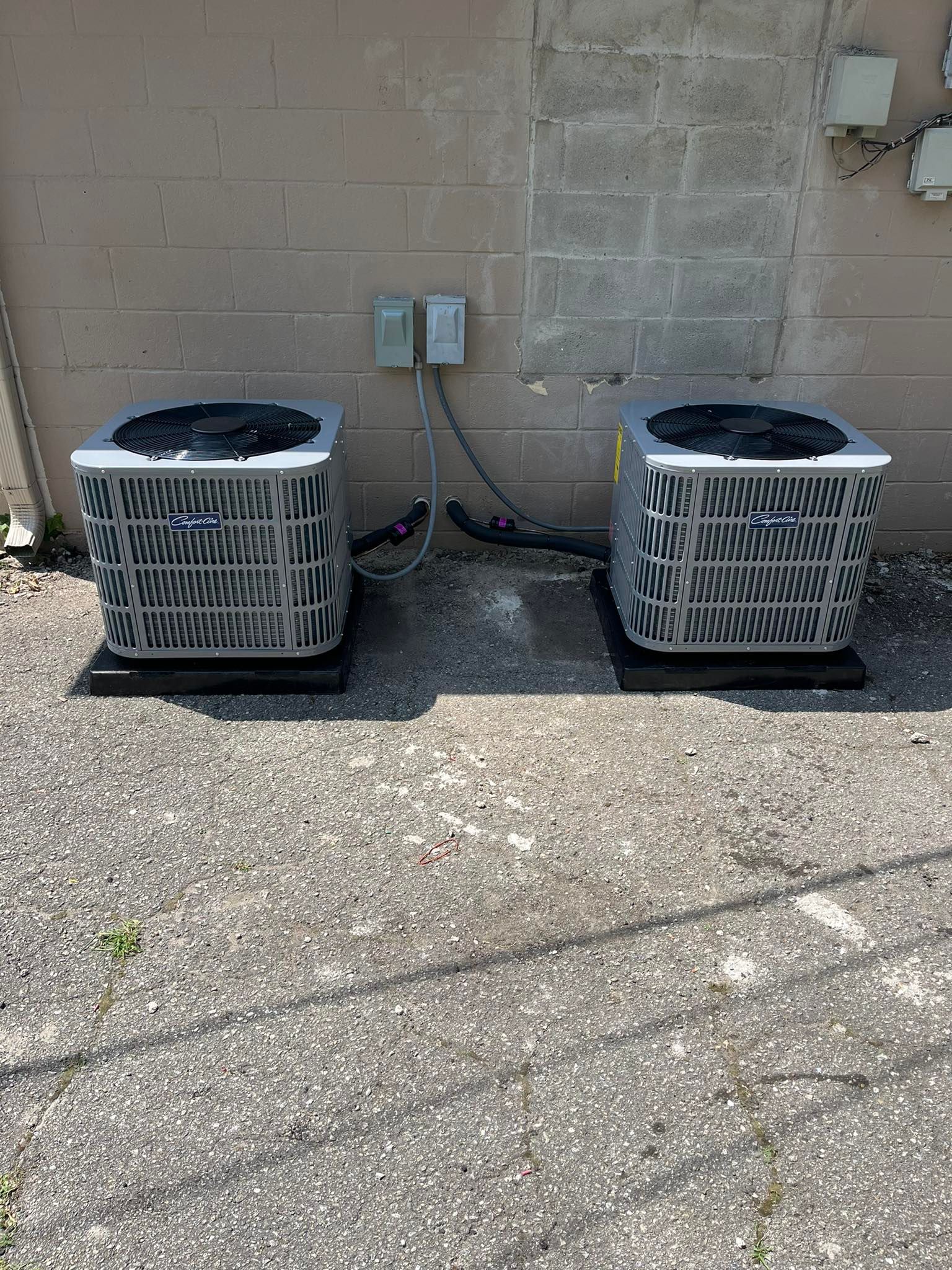 Two air conditioners are sitting next to each other on the side of a building.