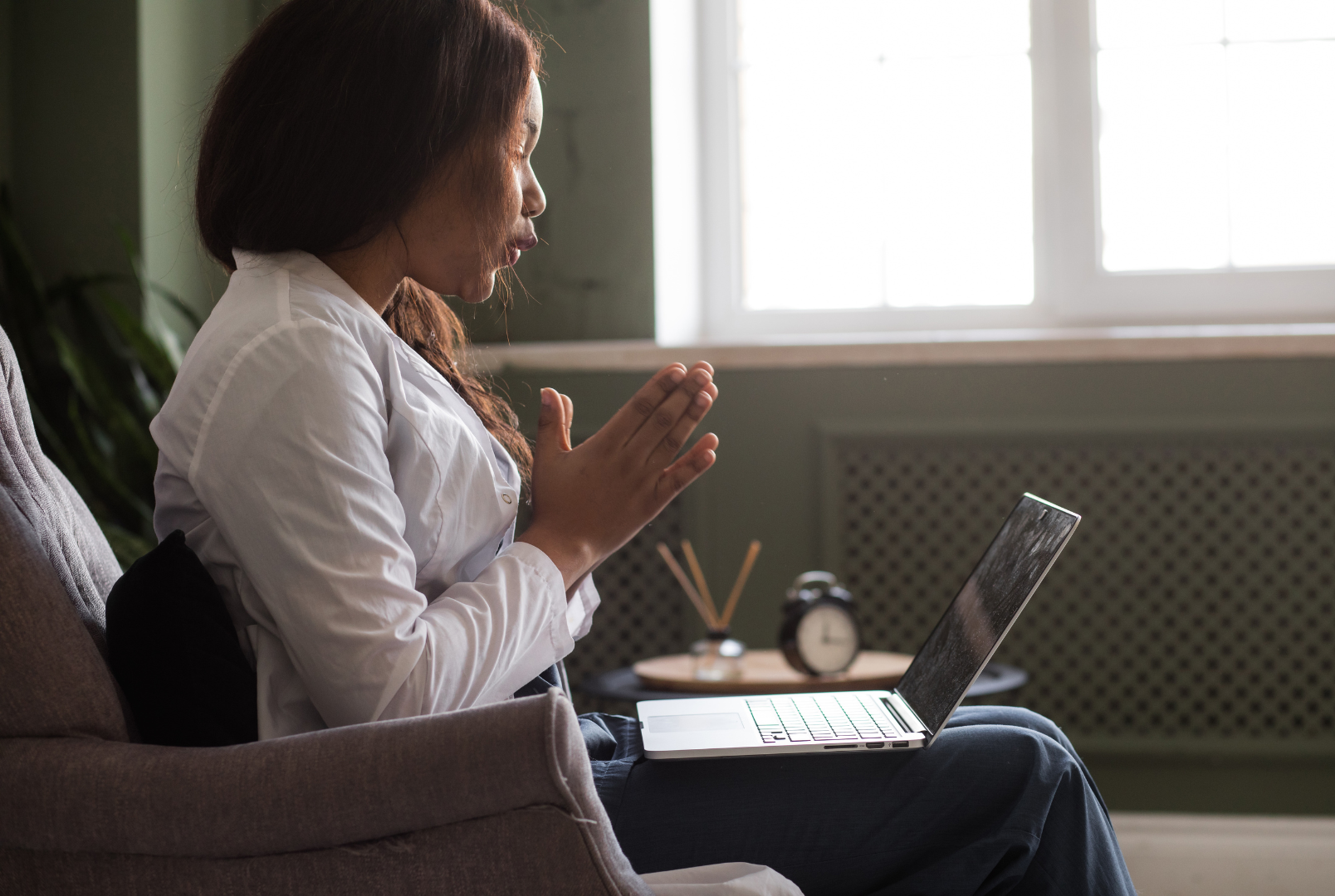 A woman is sitting in a chair with a laptop on her lap.