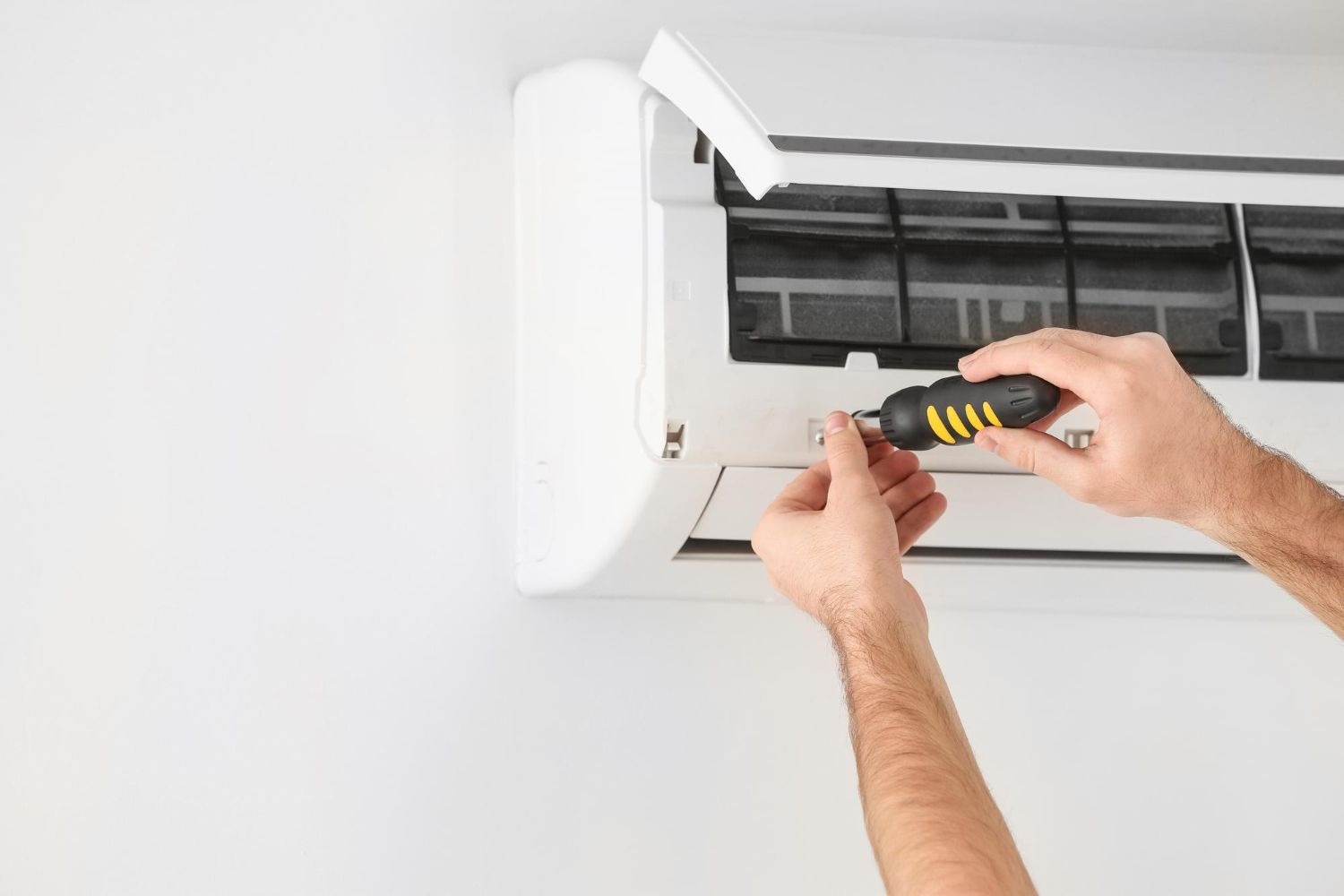 Hands using a screwdriver to repair a wall-mounted air conditioner unit
